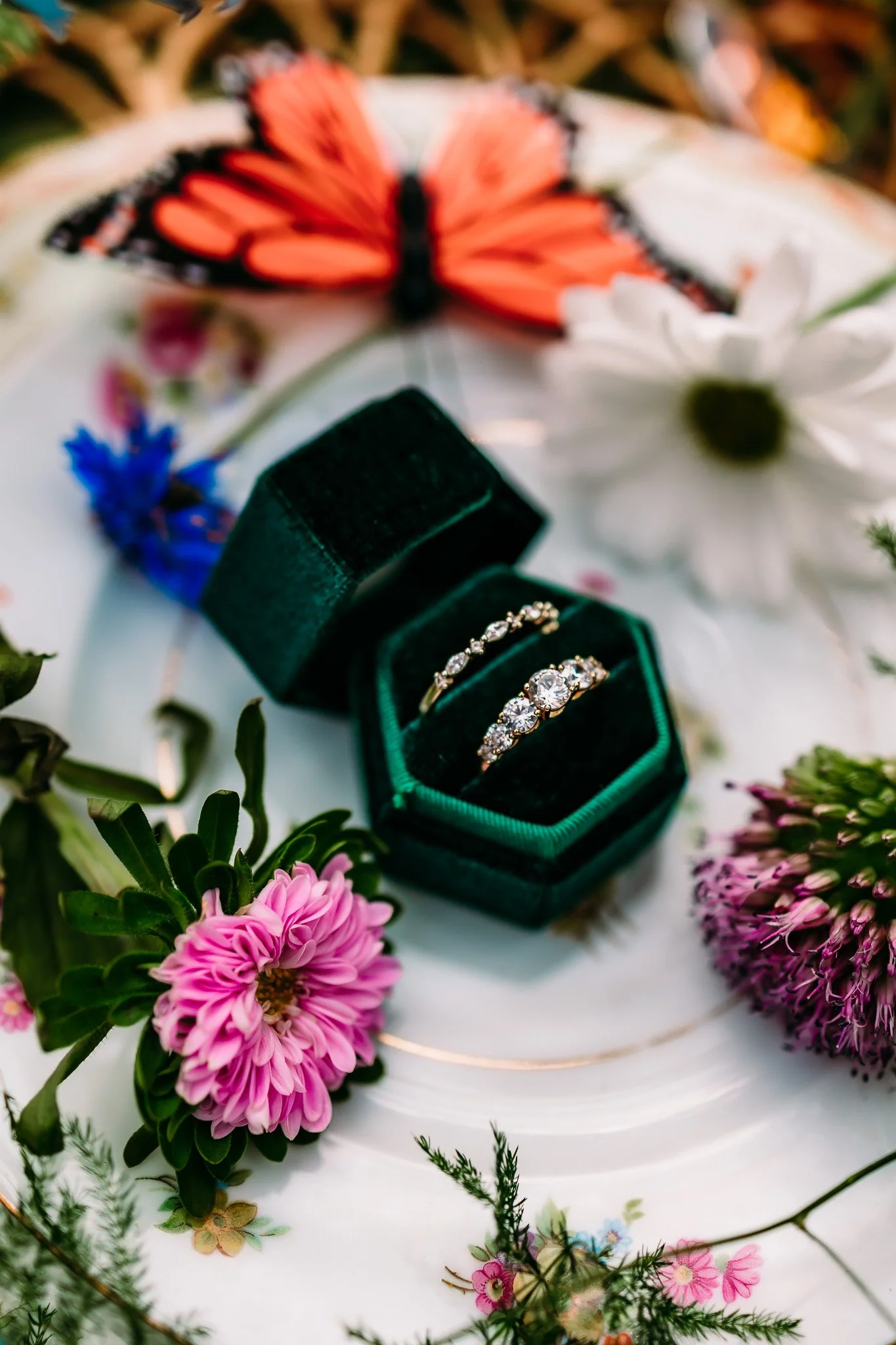 Wedding rings displayed in a velvet ring box surrounded by wildflowers and a monarch butterfly for an elopement at The Vaughn House in Forest, Virginia.