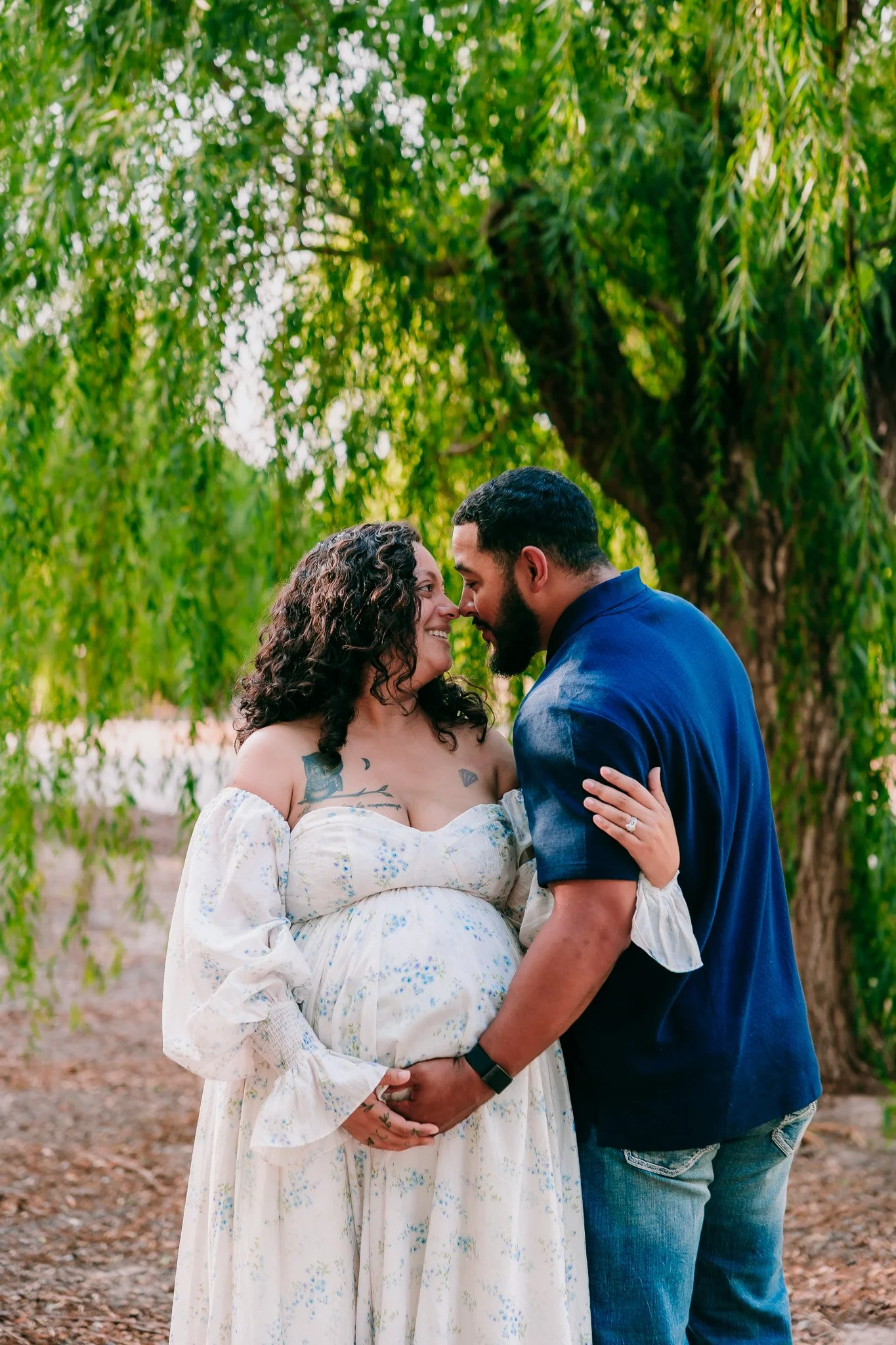 Expecting parents sharing an intimate embrace beneath the willow trees during a maternity photography session in Las Cruces.