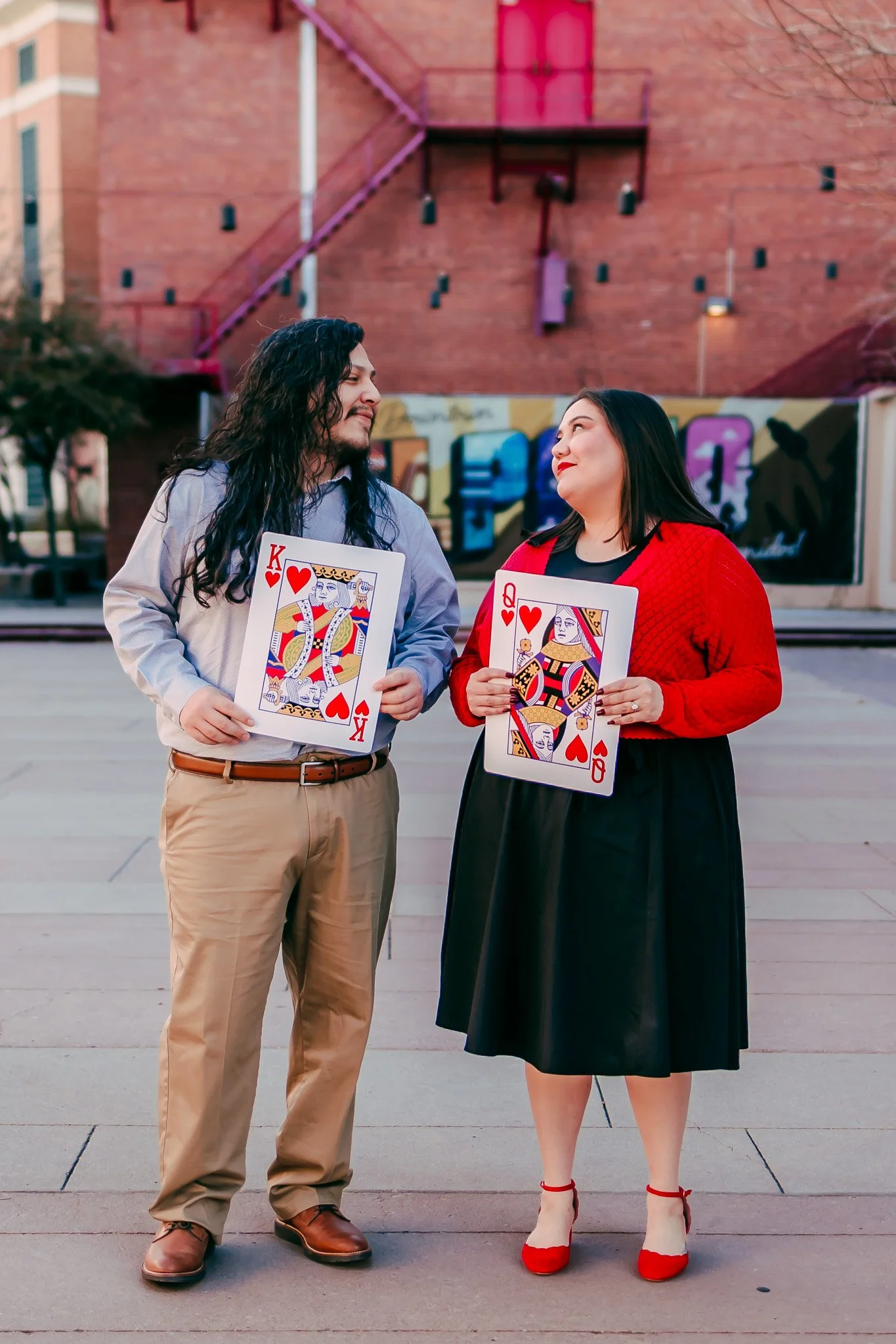 LGBTQ+ couple laughing together with oversized playing cards during a fun downtown El Paso engagement photography session.
