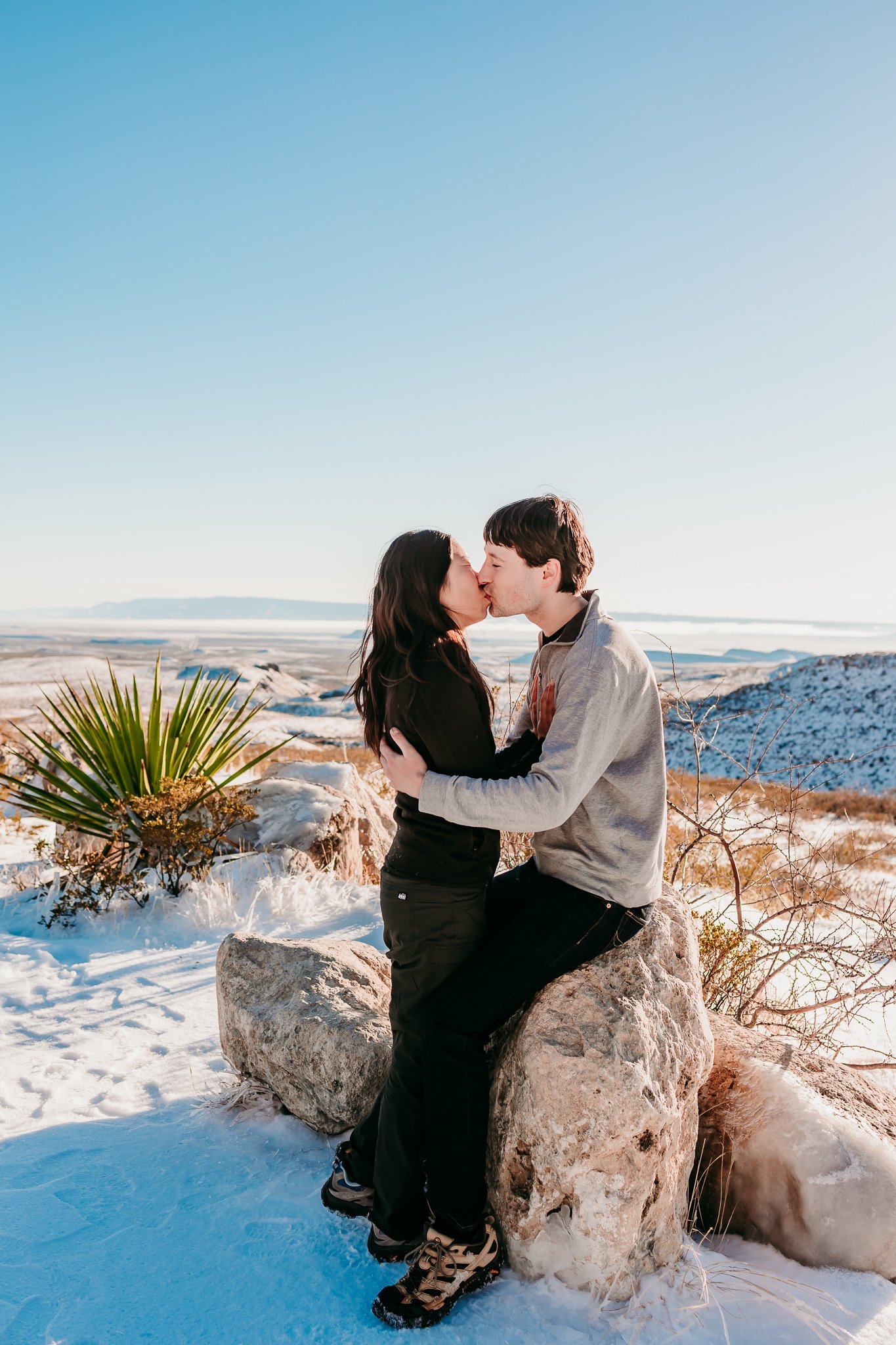 Newly engaged couple sharing a kiss on snowy desert rocks during a surprise proposal at the Guadalupe Mountains near Carlsbad, New Mexico.