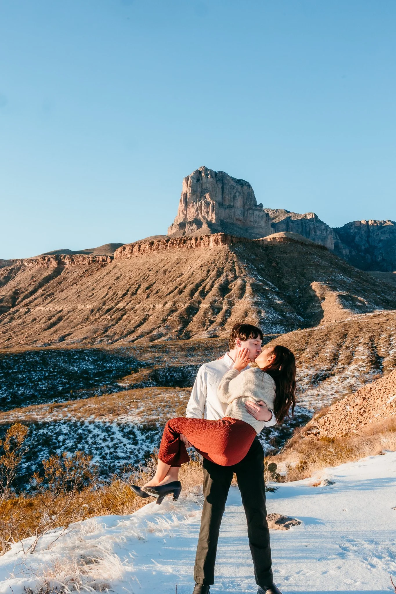 Couple celebrating their surprise engagement with a joyful lift against the Guadalupe Mountains near Carlsbad, New Mexico.