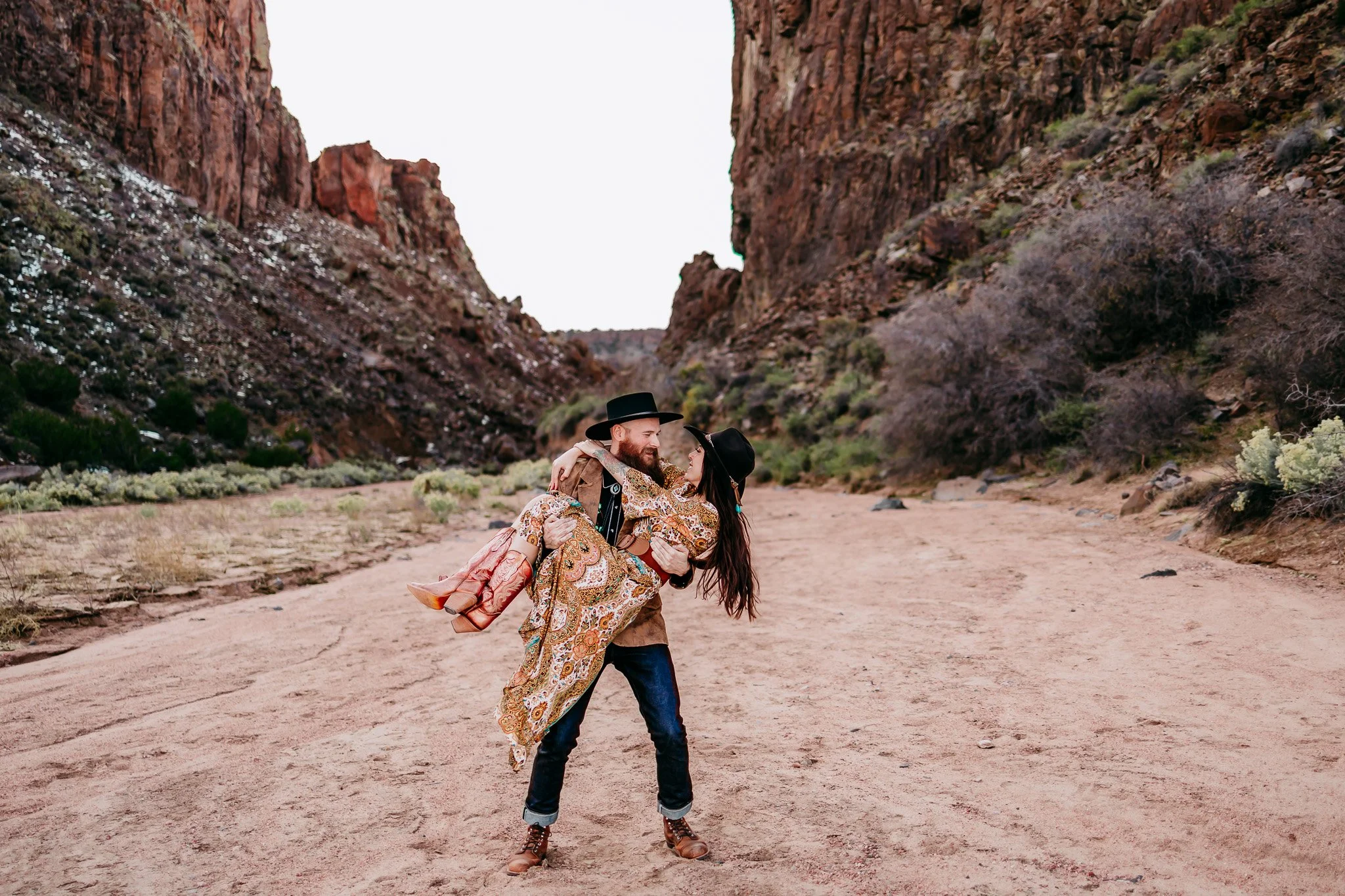 Partners embracing in front of the rugged sandstone landscape during an adventurous couples photography session in Diablo Canyon, New Mexico.
