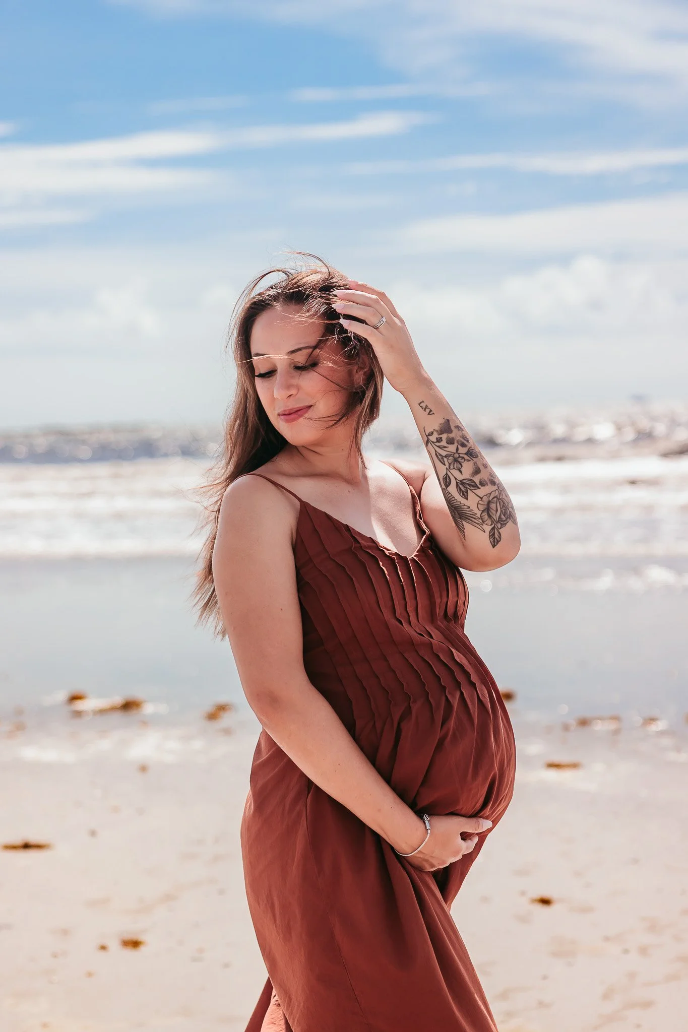 Expecting mother smiling during a natural maternity portrait on Jacksonville Beach at sunset.