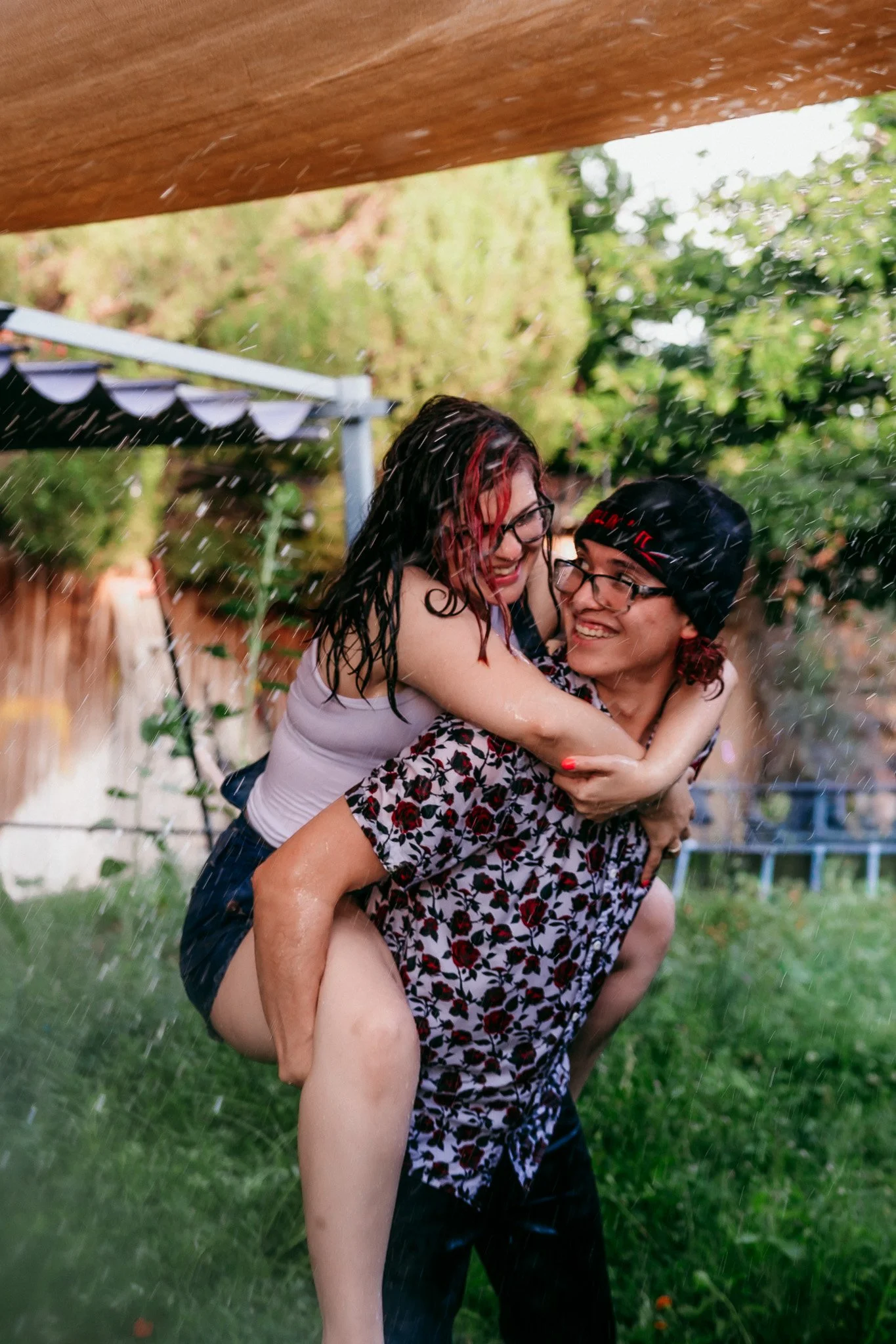 Couple laughing together during a piggyback ride in their backyard garden during an in-home couples session in Las Cruces, New Mexico.