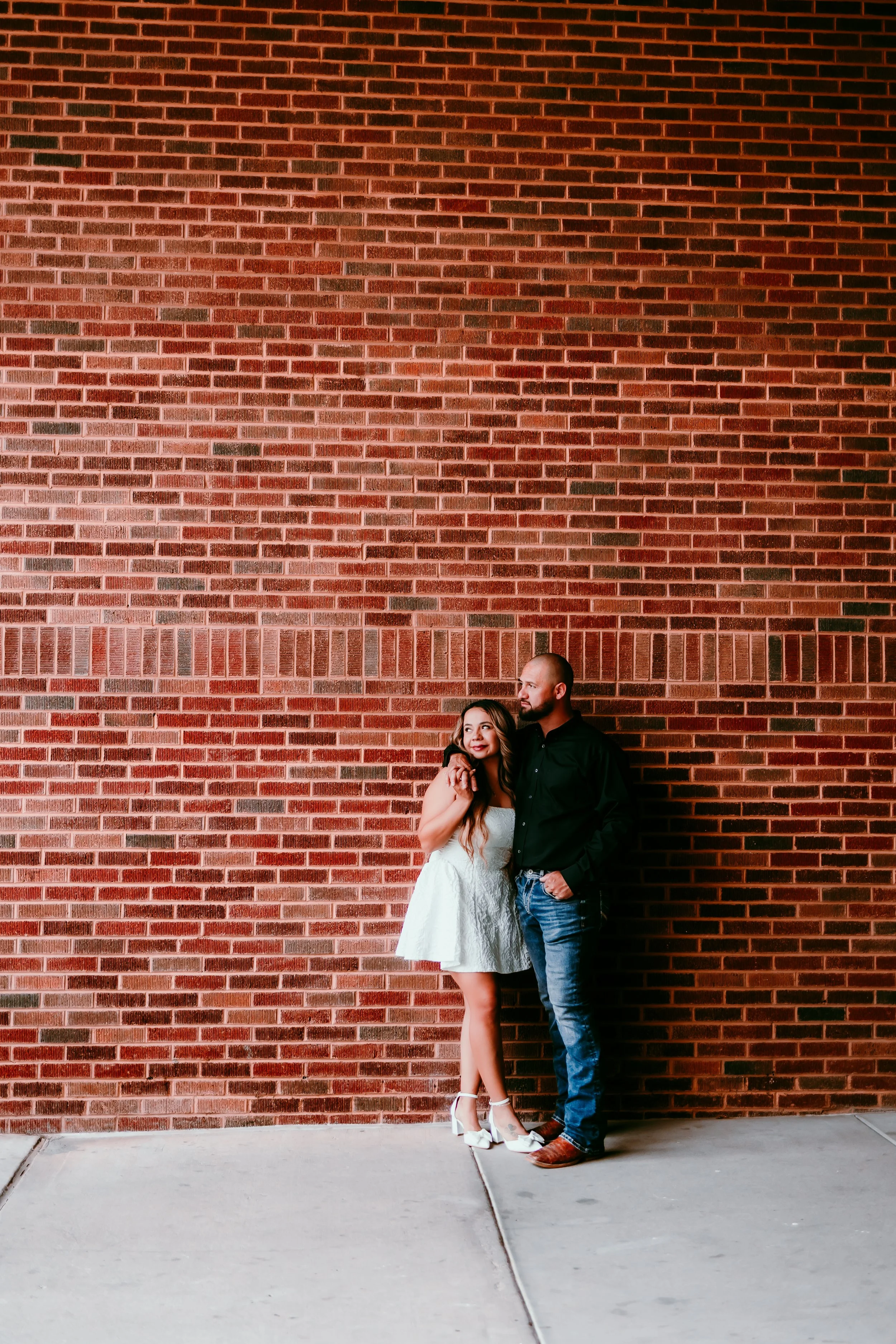 Couple laughing together against a brick wall during an urban engagement session in downtown El Paso, Texas.