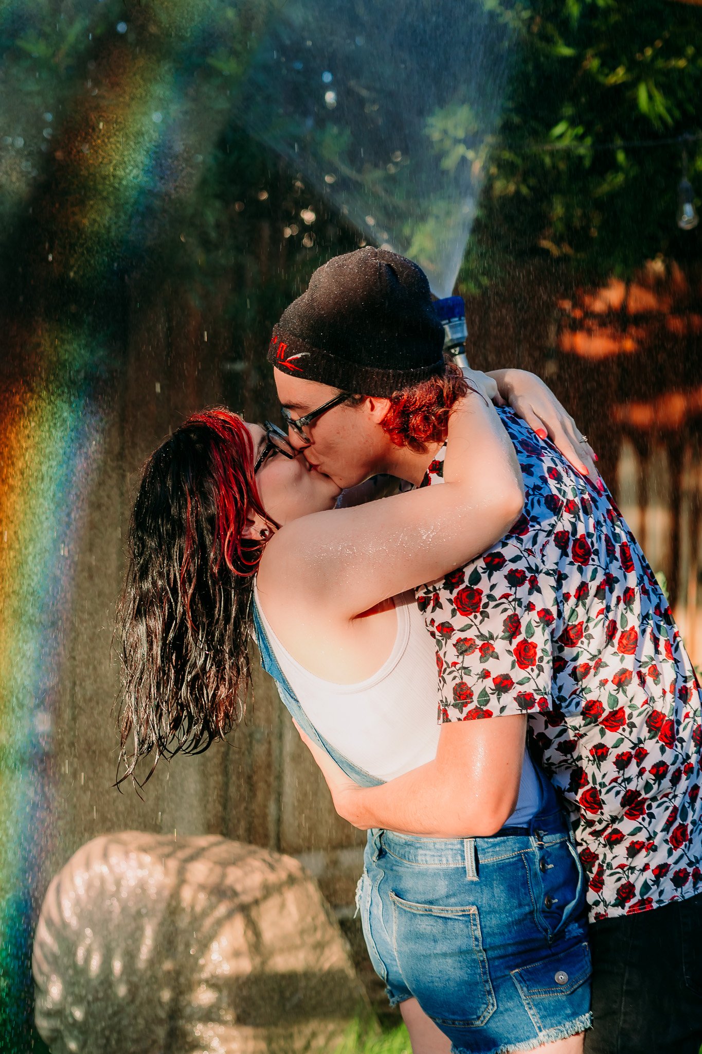 A couple kissing while spraying a water hose above their head casting a rainbow in the spray. El paso wedding photographer