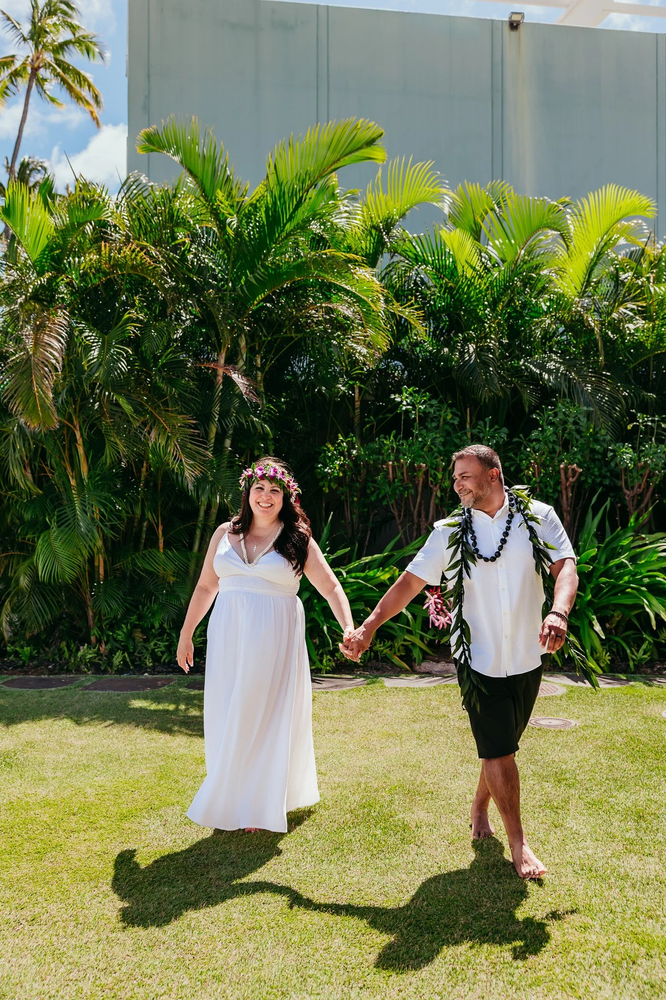 Bride and groom walking hand in hand through a tropical landscape during their Oahu, Hawaii elopement.