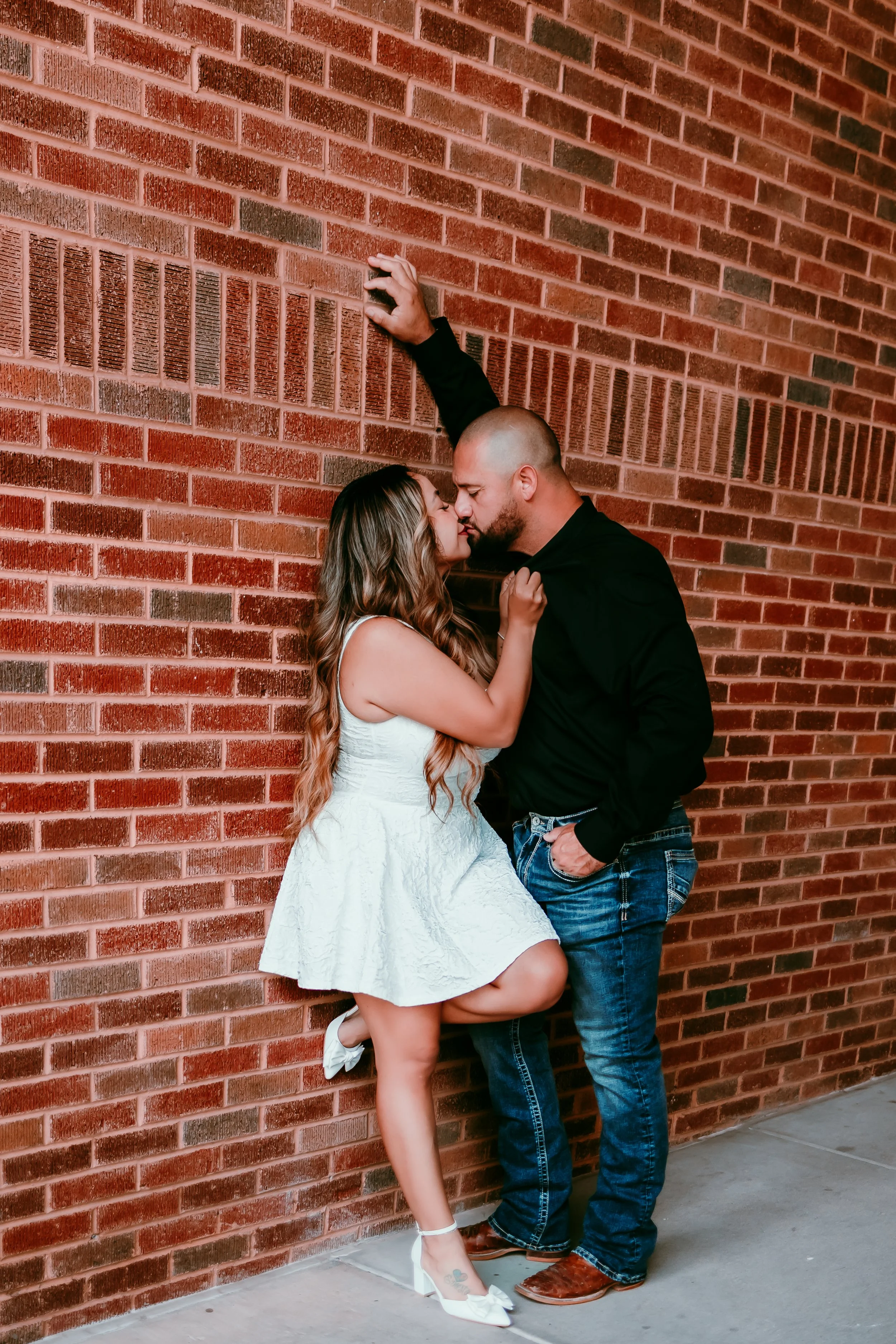 Couple embracing against a historic brick wall during a romantic engagement session in downtown El Paso.