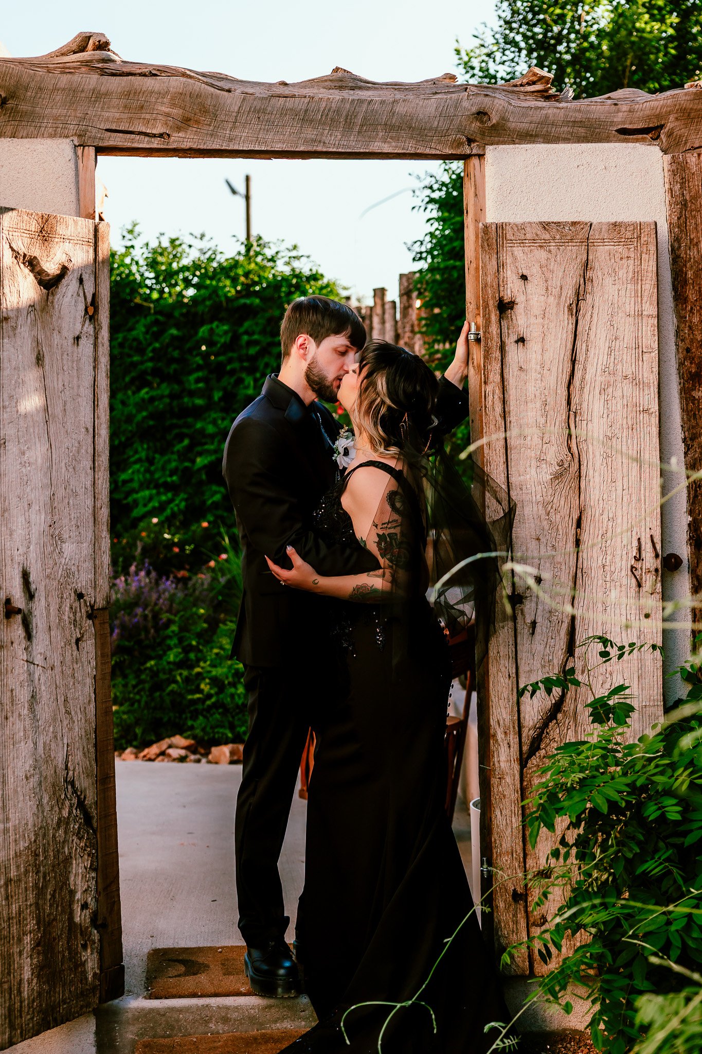 Bride and groom sharing a kiss beneath a rustic wooden gate at The Mystic during their intimate Santa Fe wedding.