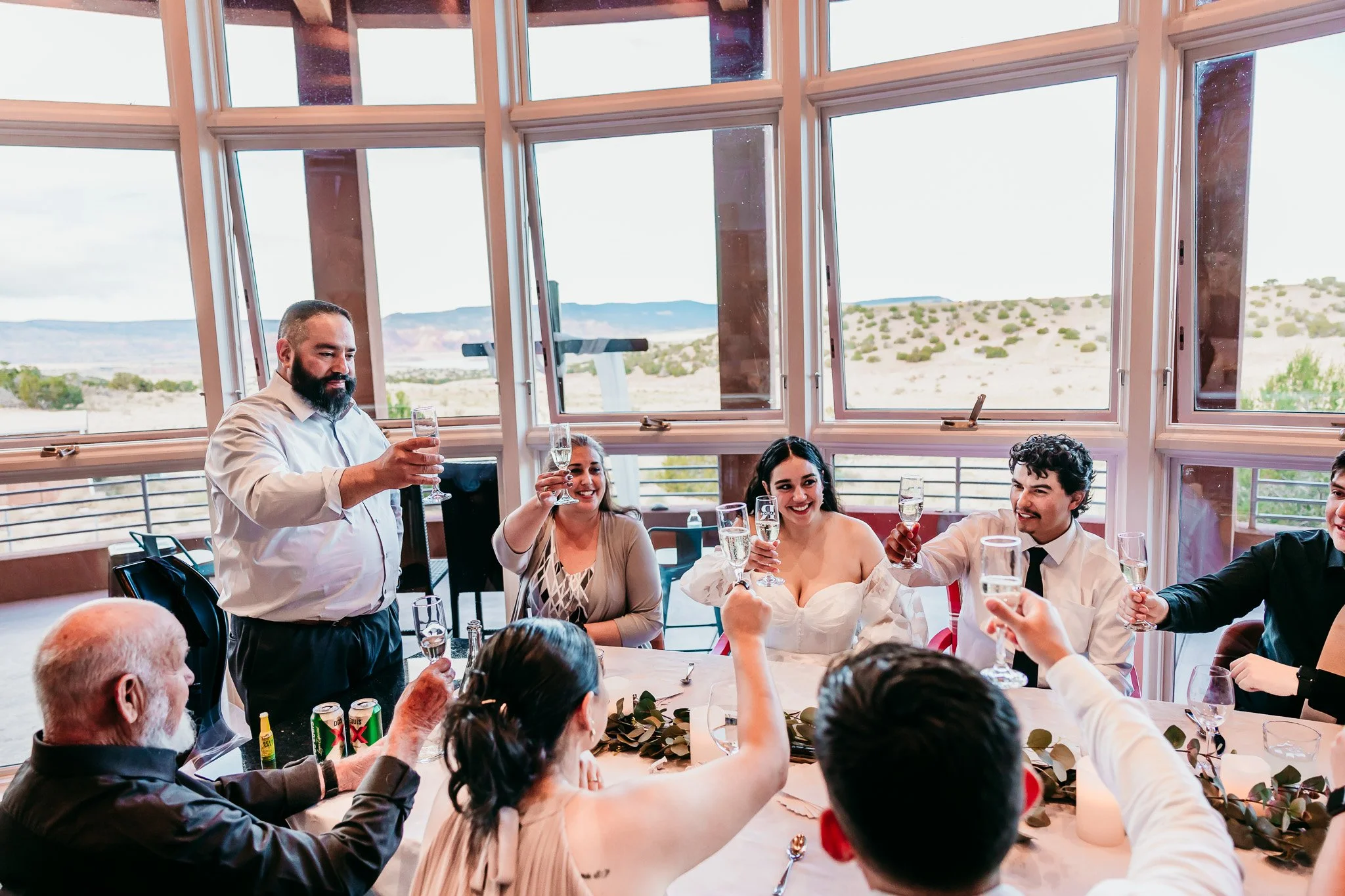 Bride, groom, and their family raising champagne glasses during a private elopement reception with scenic views of Abiquiu Lake in New Mexico.