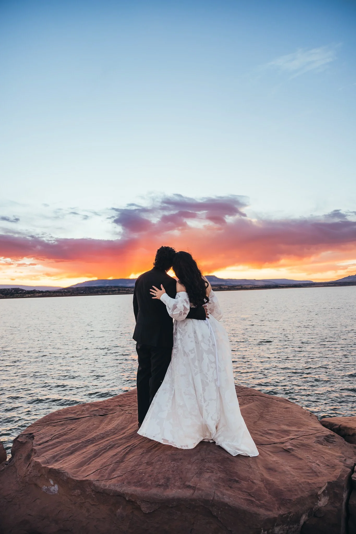 Bride and groom embracing on the rocky shoreline during a sunset elopement at Abiquiu Lake in northern New Mexico.