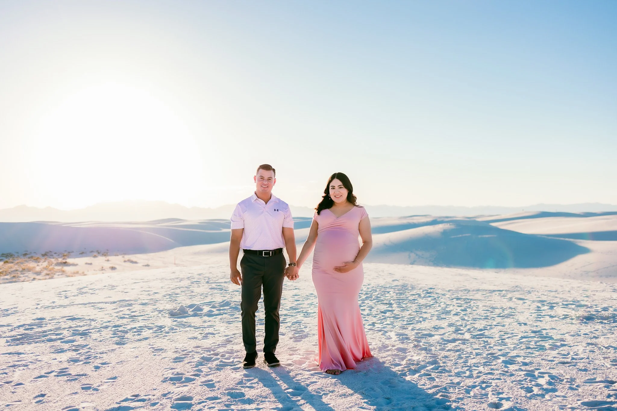 Expecting couple walking hand in hand across the dunes during a White Sands maternity session at White Sands National Park.