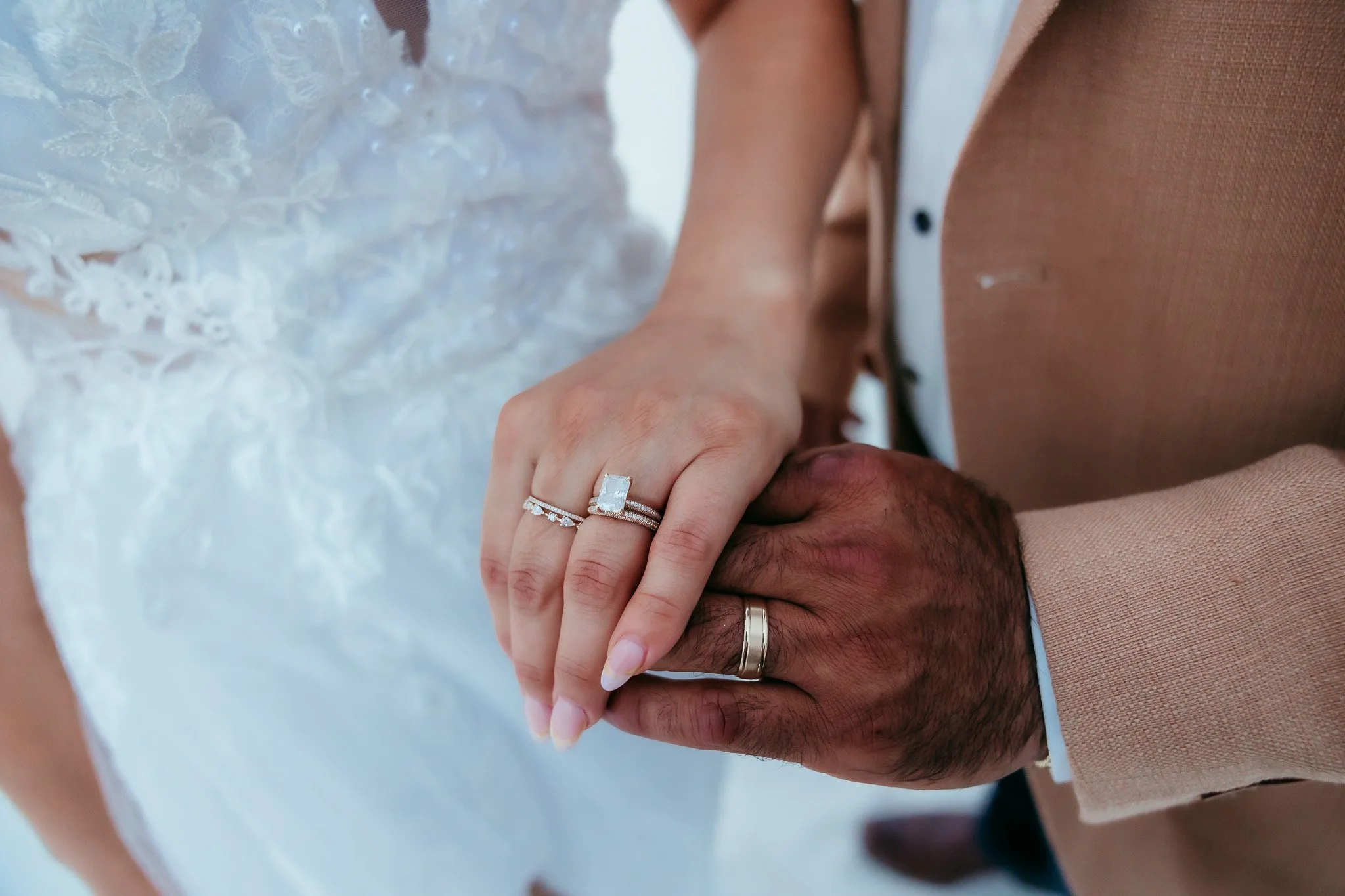 Close-up of bride and groom's wedding rings while holding hands against the white dunes during their White Sands National Park elopement in New Mexico.