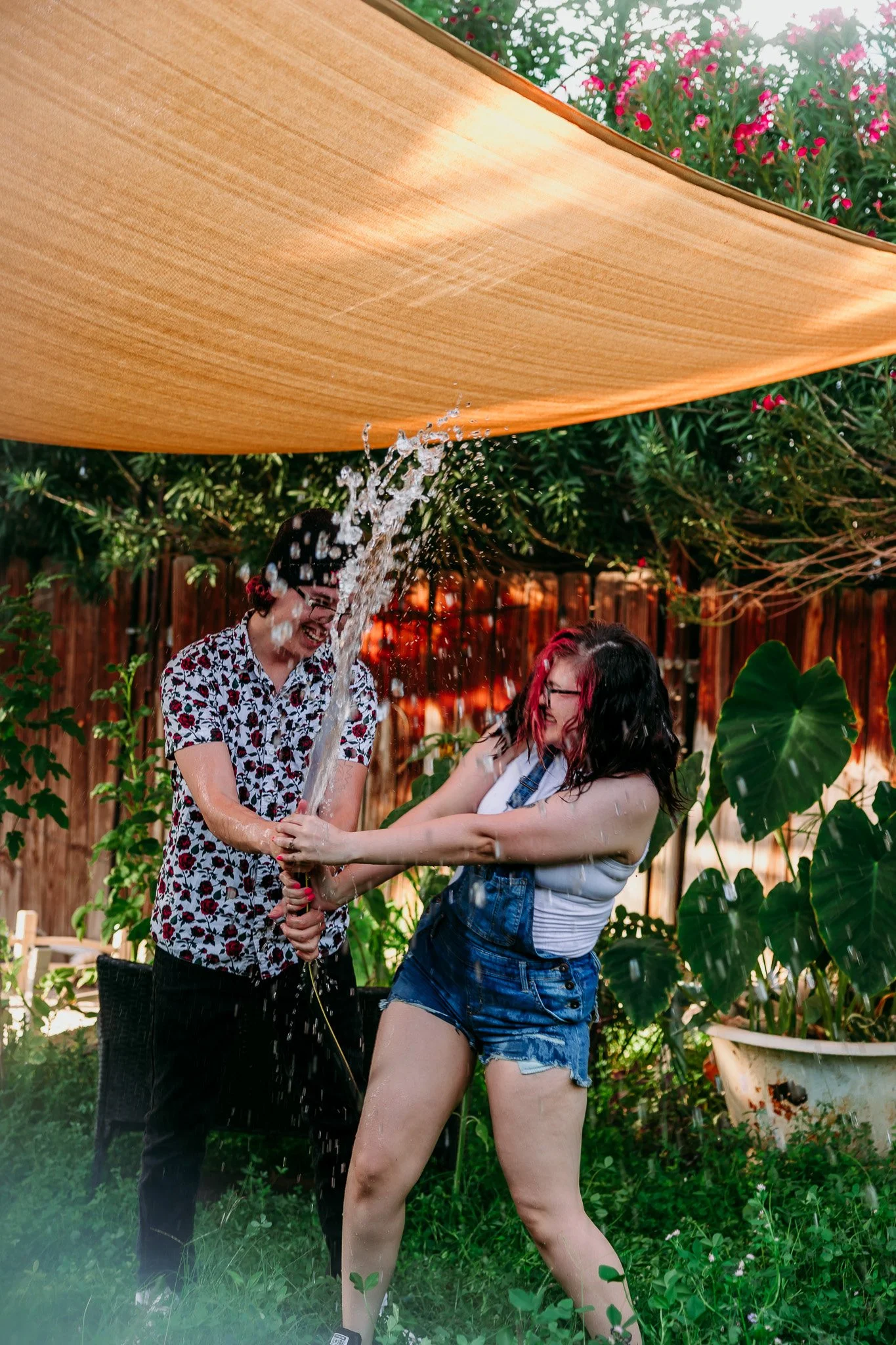 Partners running through a backyard sprinkler during a fun in-home couples photography session in Las Cruces, New Mexico.