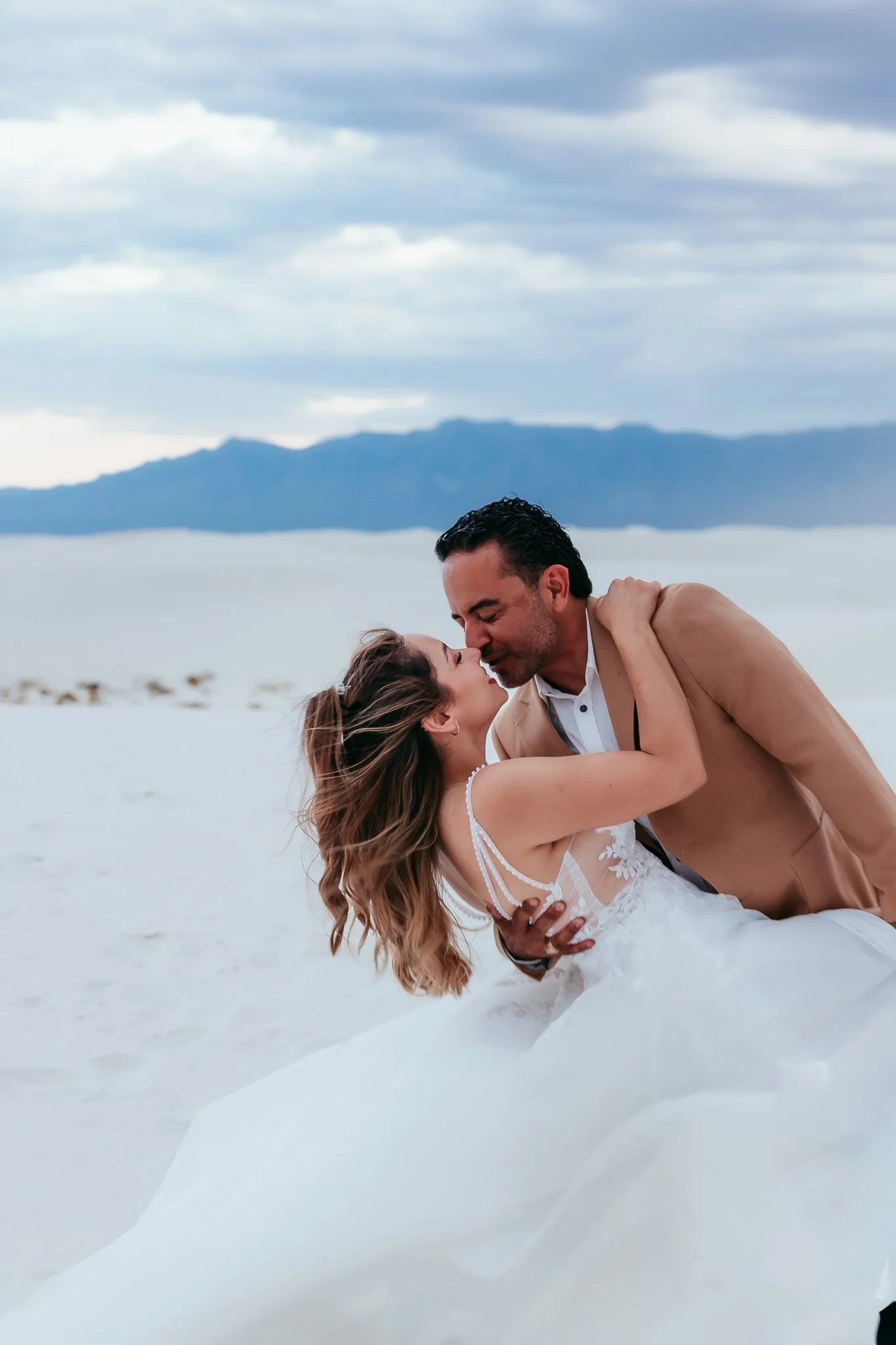 Groom holding bride with her windswept hair flowing during a romantic portrait session at White Sands National Park in New Mexico.