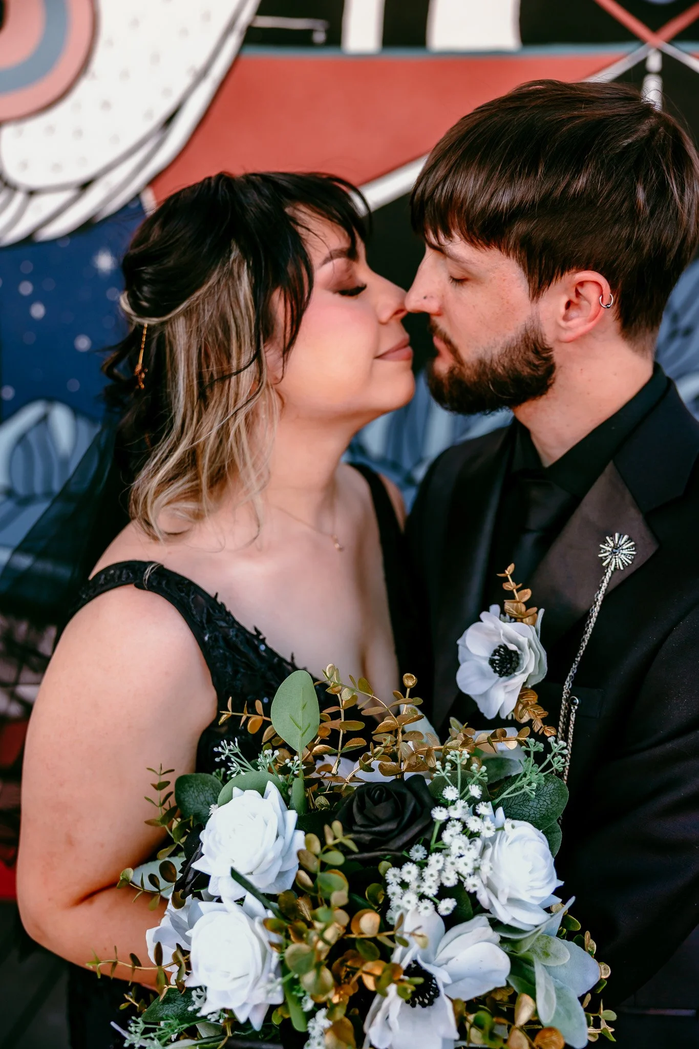 Bride and groom sharing a romantic forehead kiss with a black and white bouquet in front of the colorful mural at The Mystic during their intimate Santa Fe wedding.