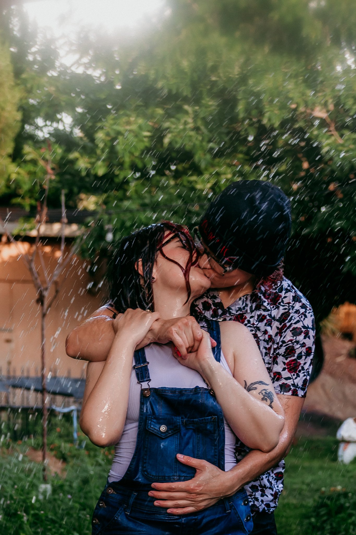 A couple hugging from behind & kissing in a backyard garden with water spraying around them. New mexico elopement photographer