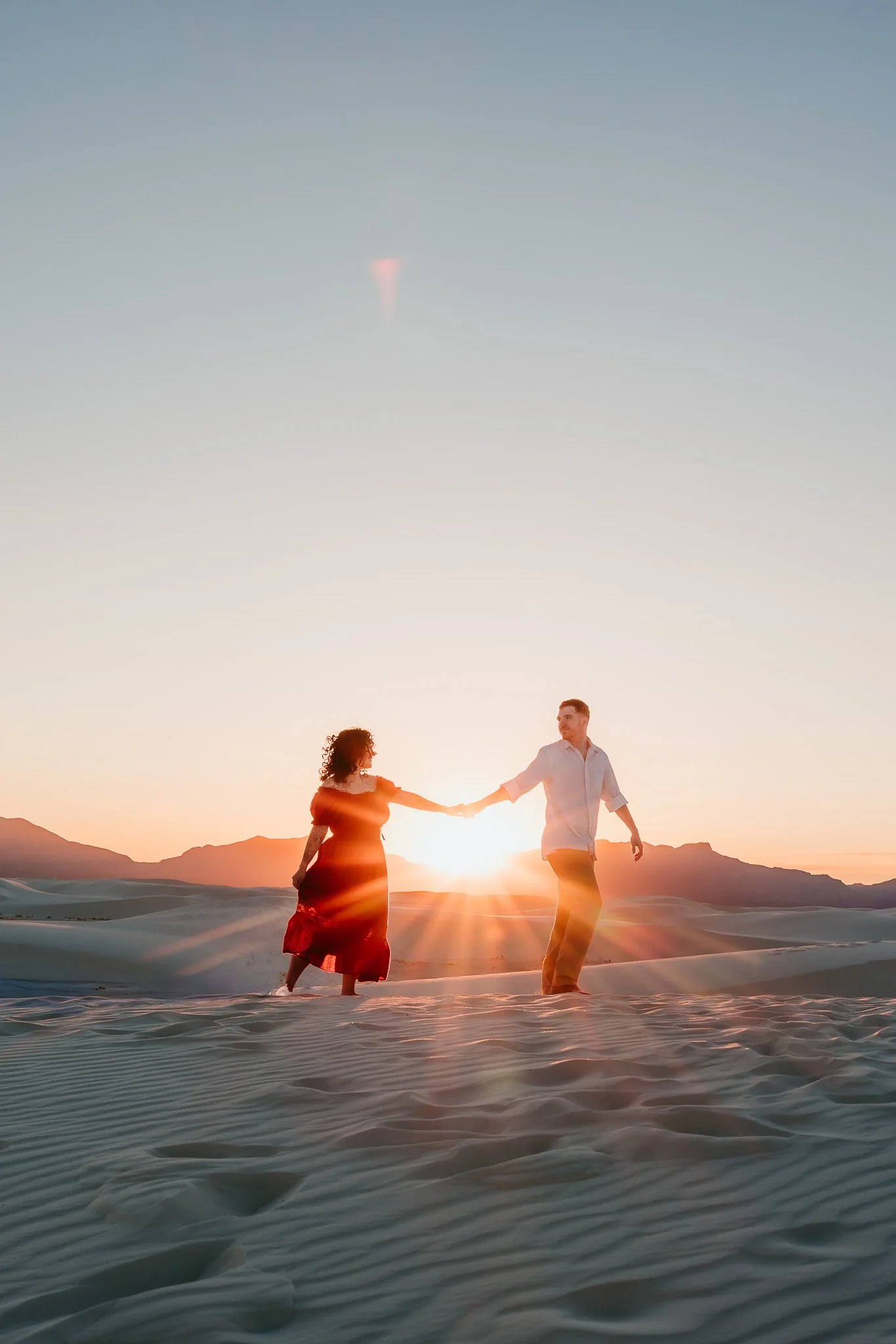 Engaged couple walking through the white gypsum dunes at golden hour during a romantic White Sands National Park engagement session.