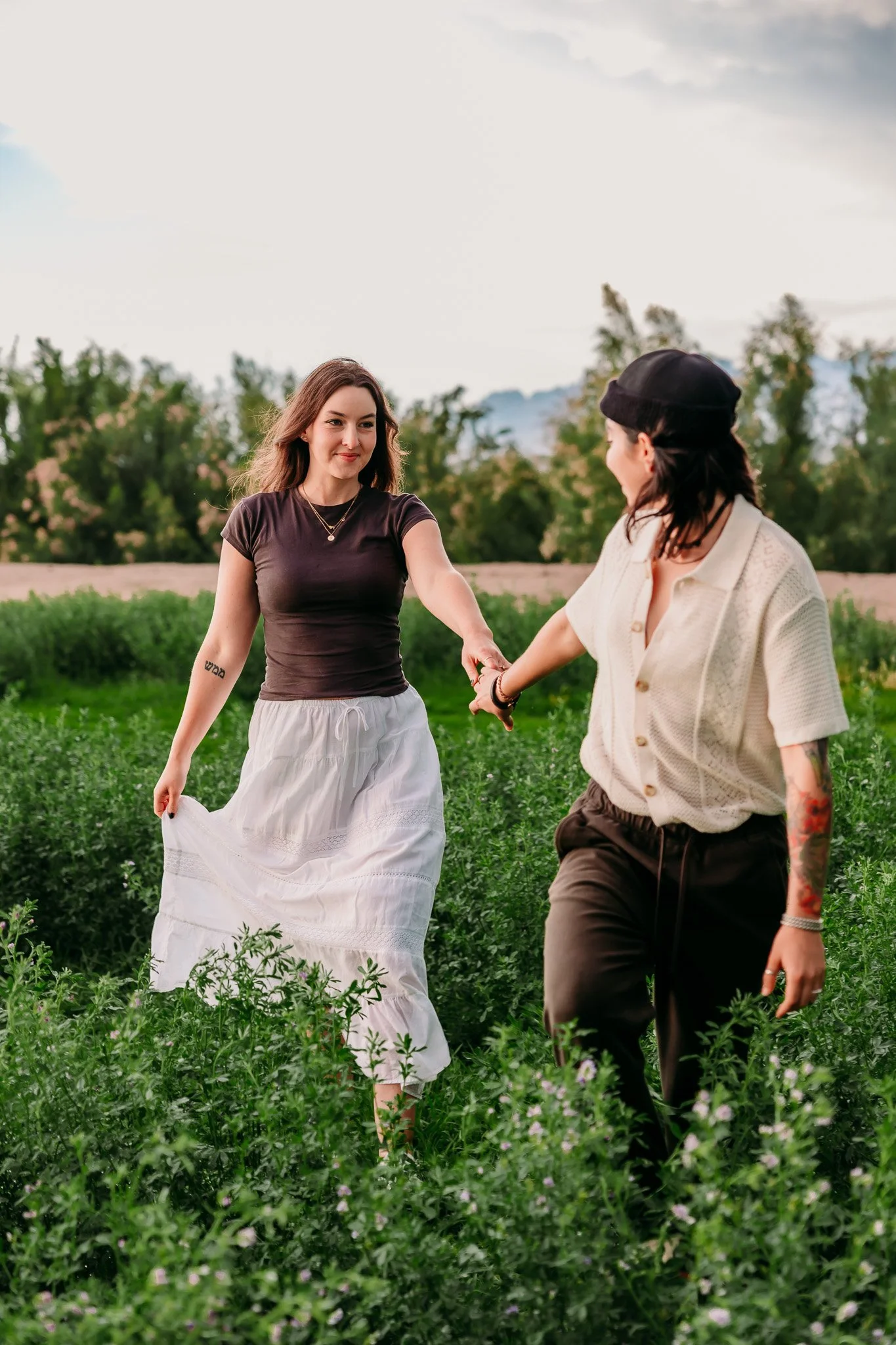 Couple holding hands while walking through a green field during a romantic couples session in Mesilla, New Mexico.