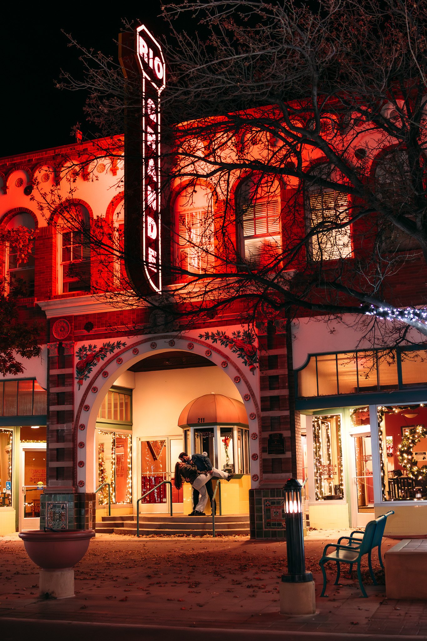 A couple kissing in front of a decorated building with a neon Rio sign at night.