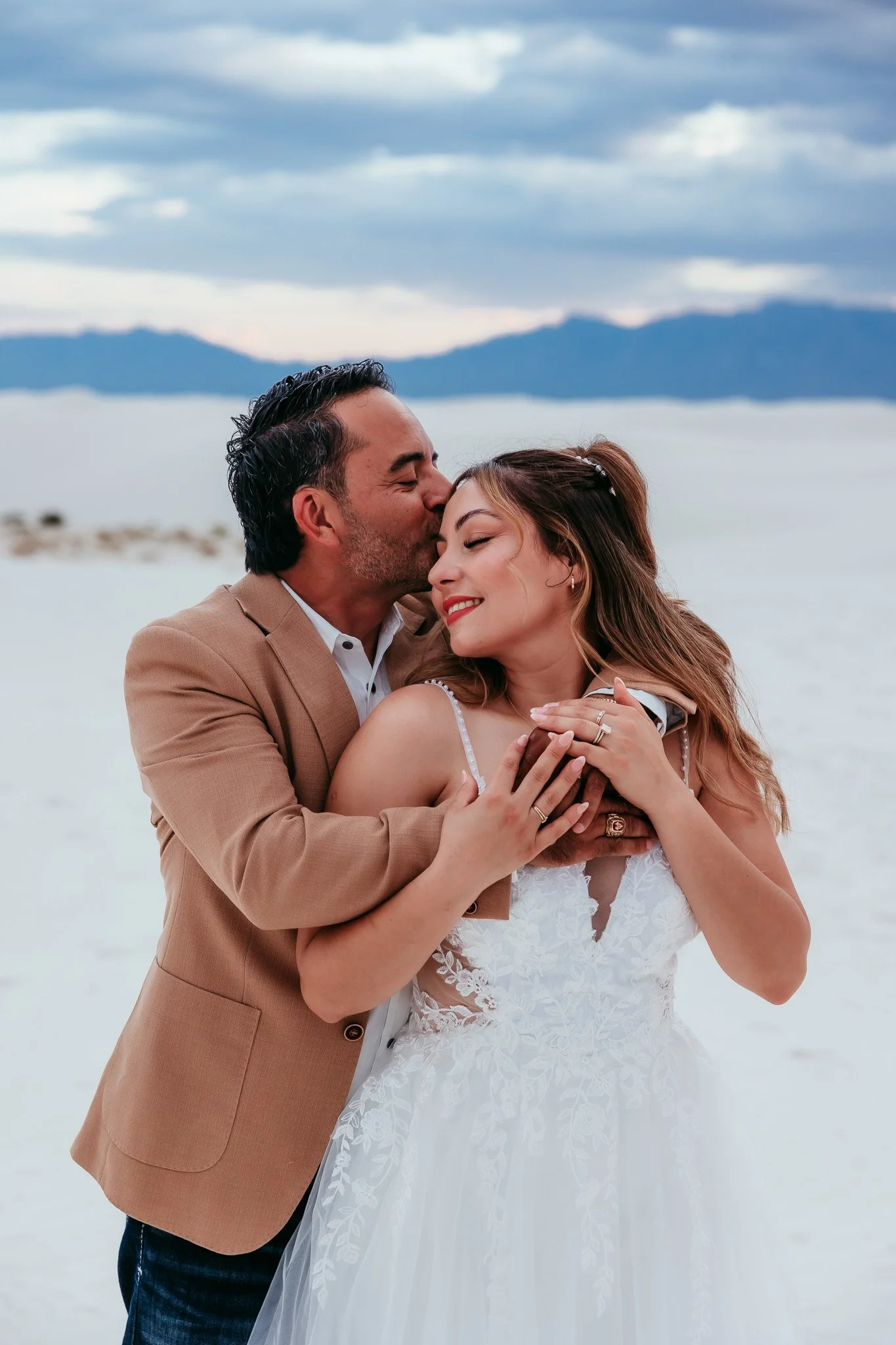 Groom holding bride with their hands overlapping to showcase their wedding rings during their White Sands National Park elopement in New Mexico.