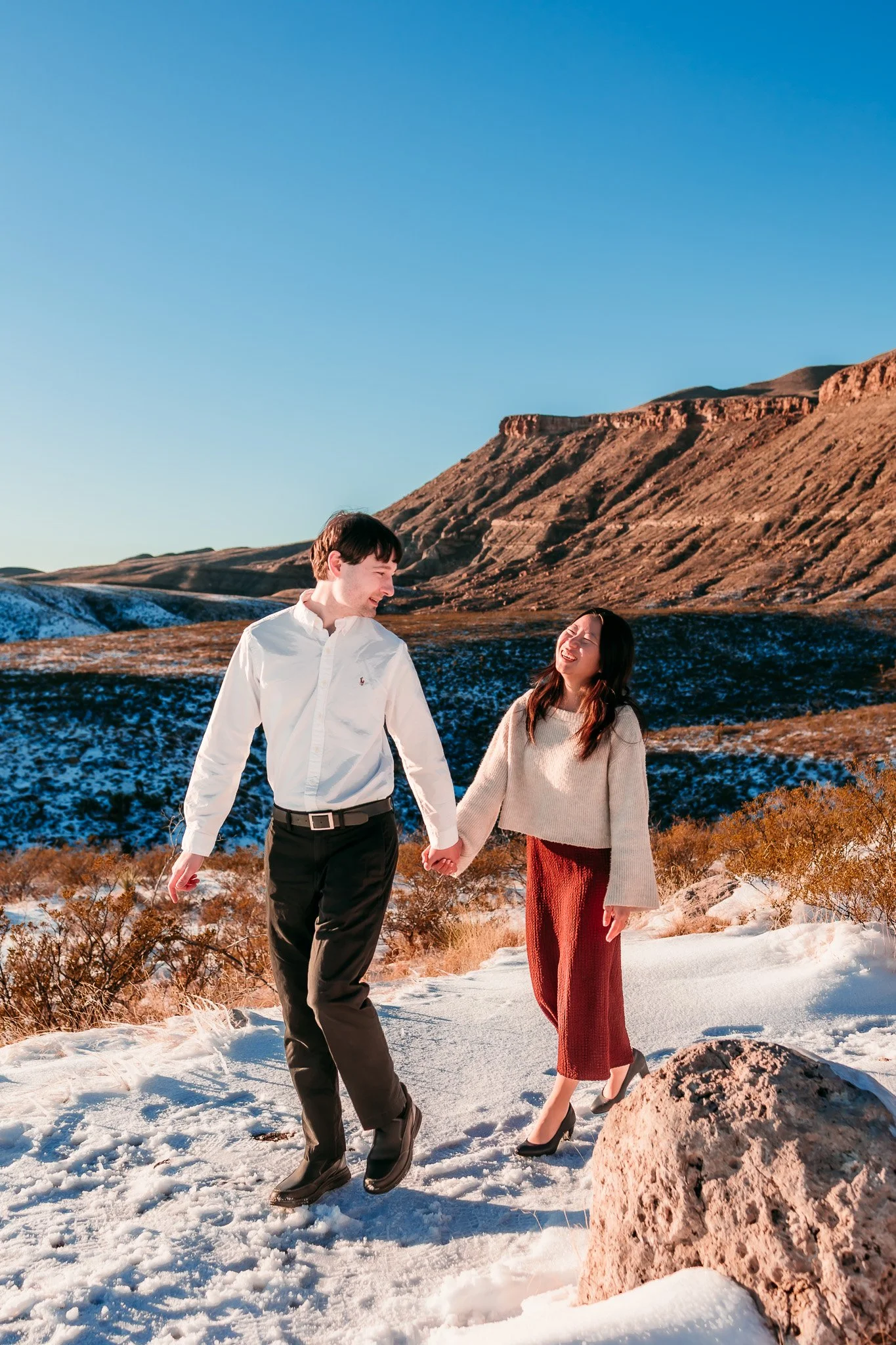 Newly engaged couple laughing together while exploring the snowy Guadalupe Mountains landscape near Carlsbad, New Mexico.
