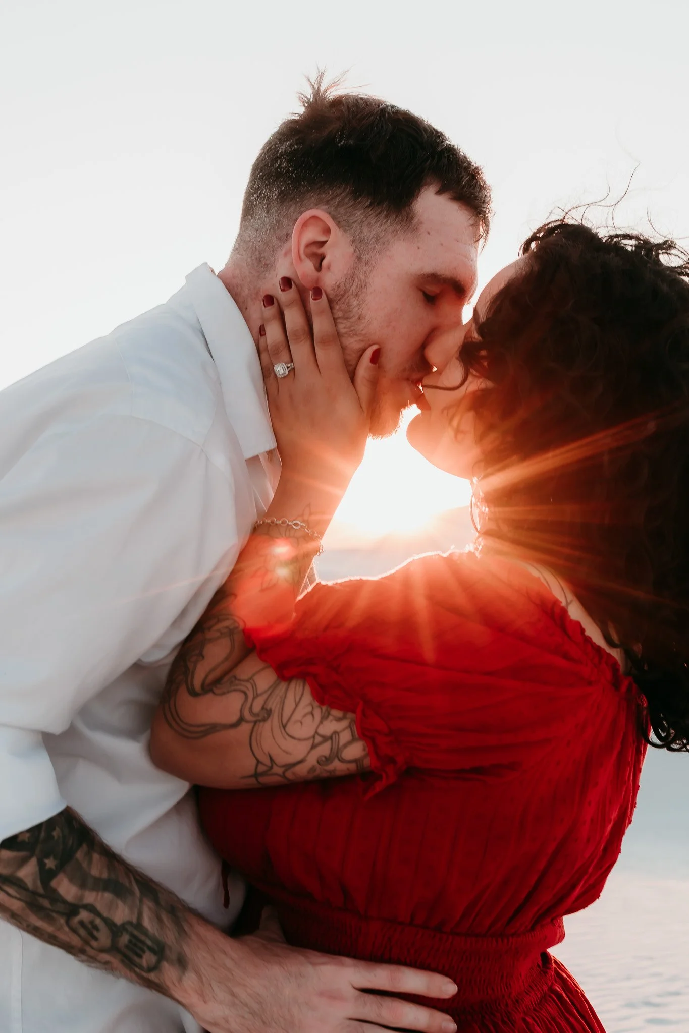 Couple kissing with the sun setting behind them during a romantic engagement session at White Sands National Park in New Mexico.