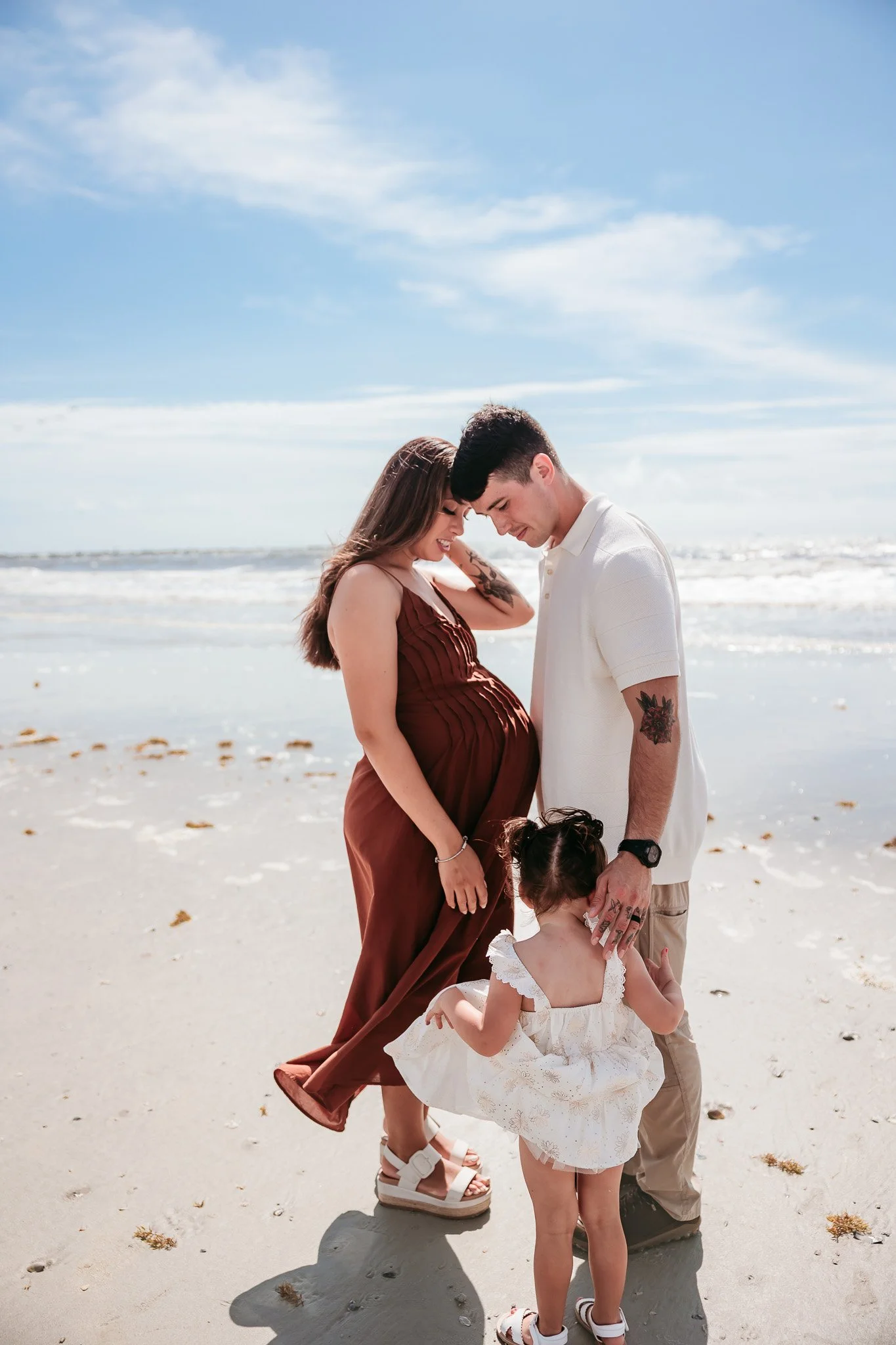 Couple embracing while their toddler stands beside them during a sunset beach maternity session in Jacksonville, Florida.