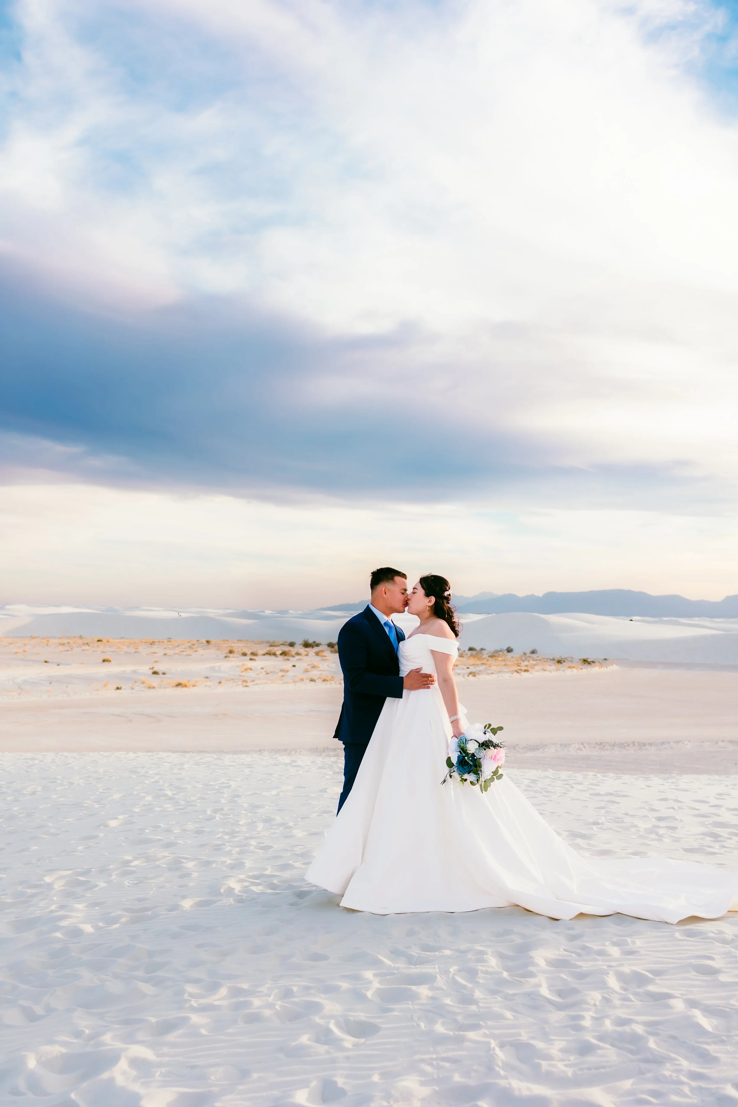 Romantic wedding portrait of bride and groom kissing at sunset in White Sands National Park, New Mexico.