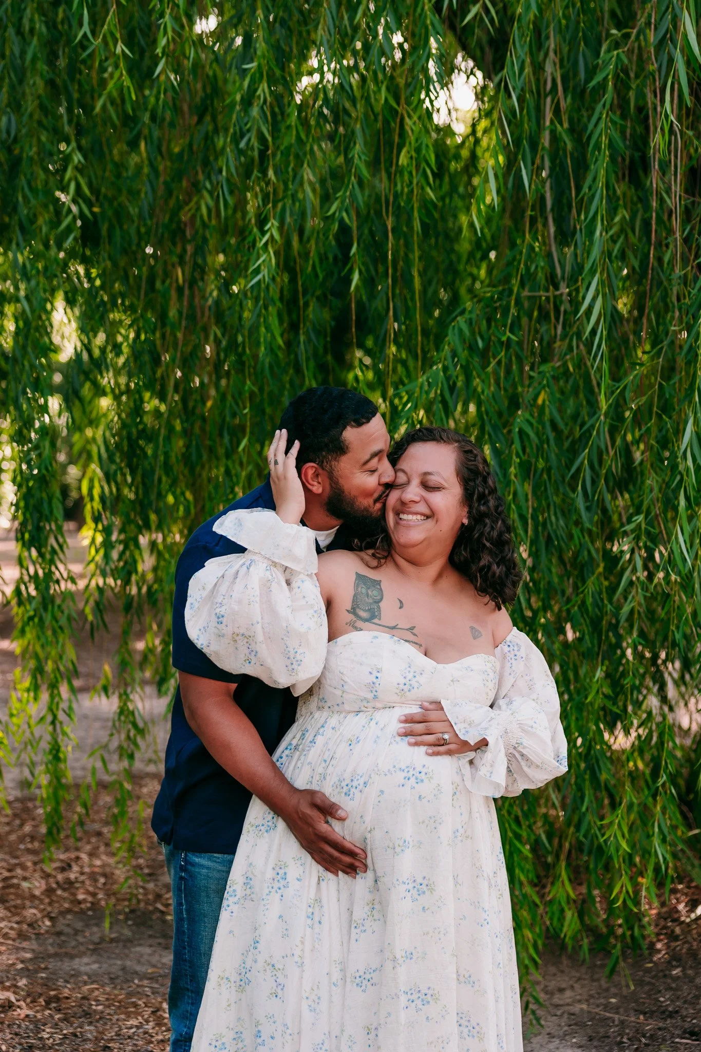 Expectant parents embracing beneath willow trees during a romantic maternity photography session in Las Cruces.