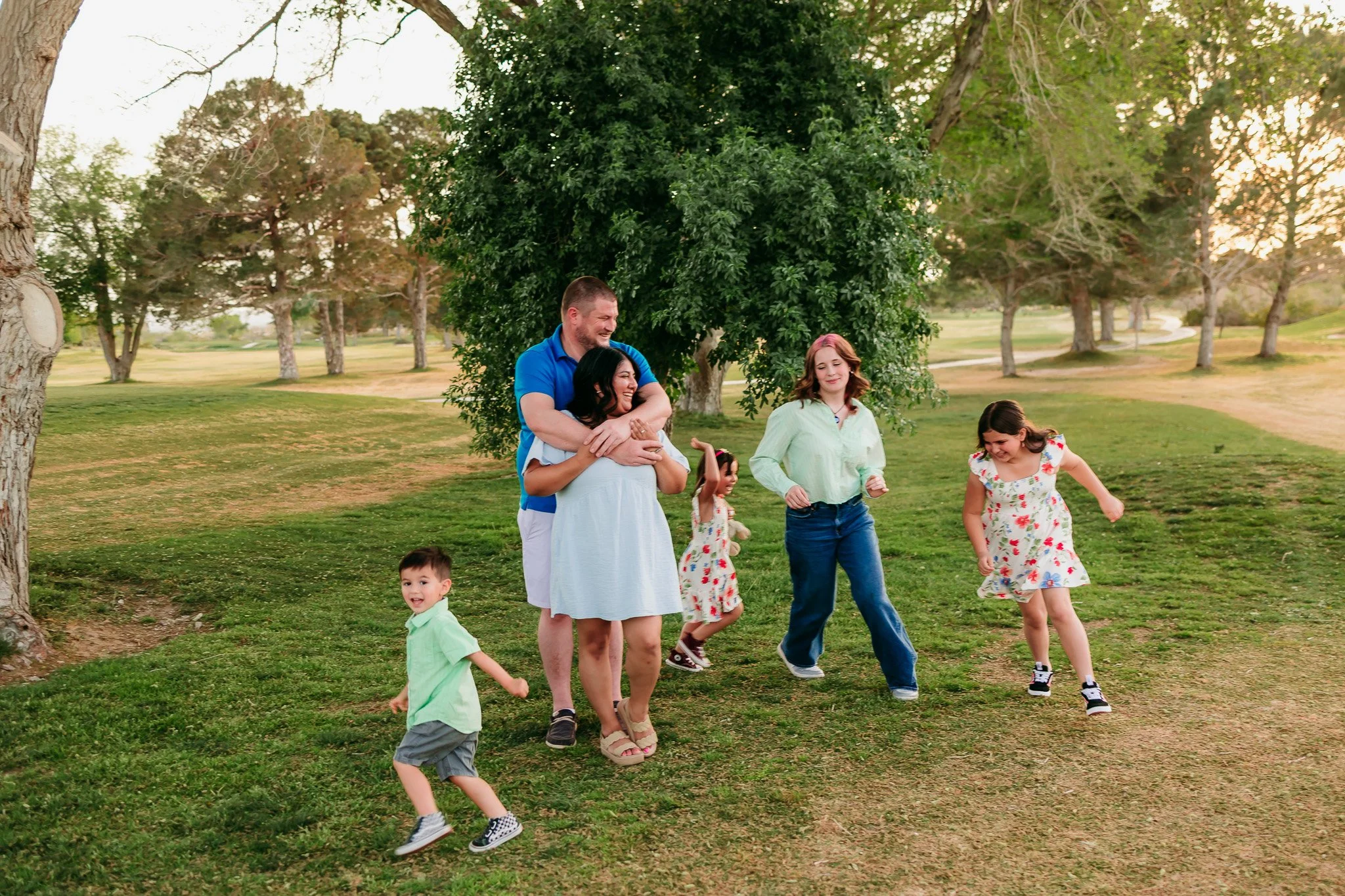 Family walking together across the grass at sunset during a candid family photography session at NMSU Golf Course. New Mexico family photographer