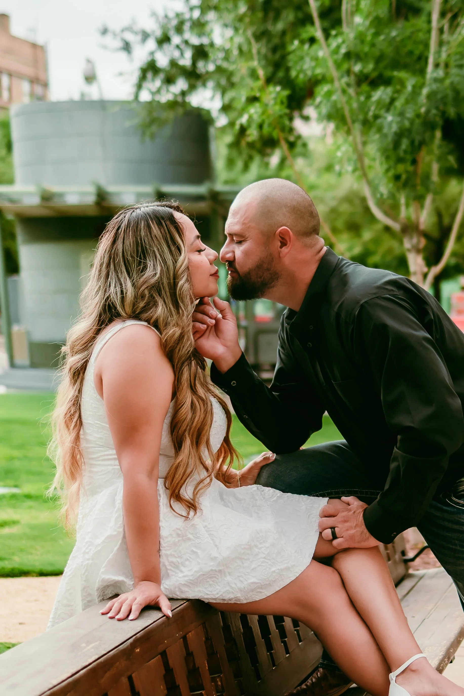 Engaged couple sharing a kiss in a downtown El Paso park during a natural and candid engagement photography session.