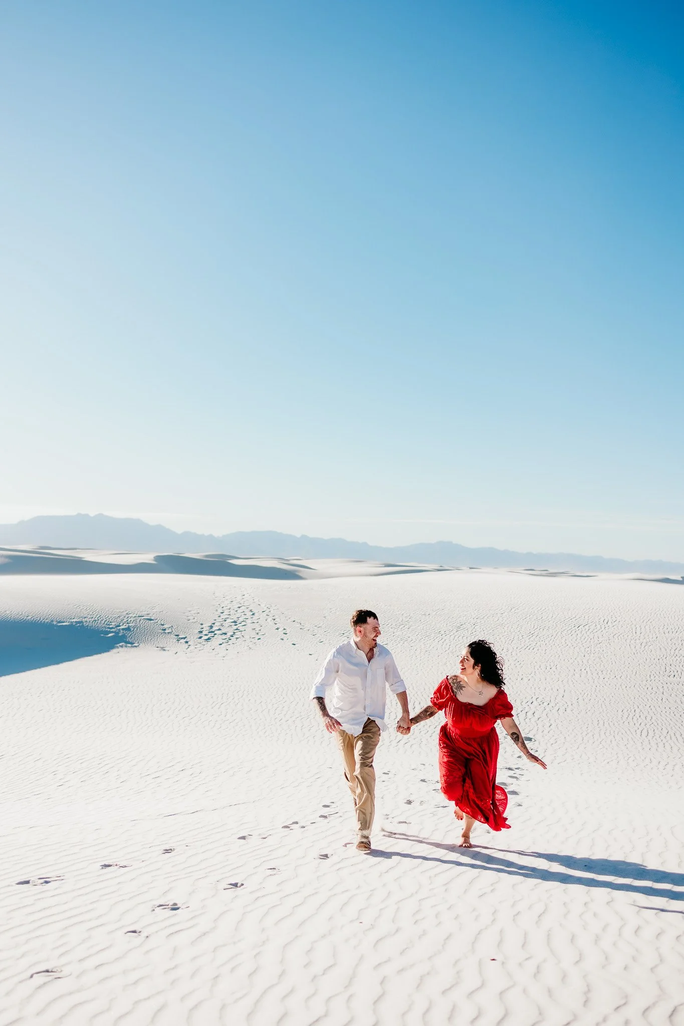 Couple running hand in hand across the white gypsum dunes during a romantic engagement session at White Sands National Park, New Mexico.