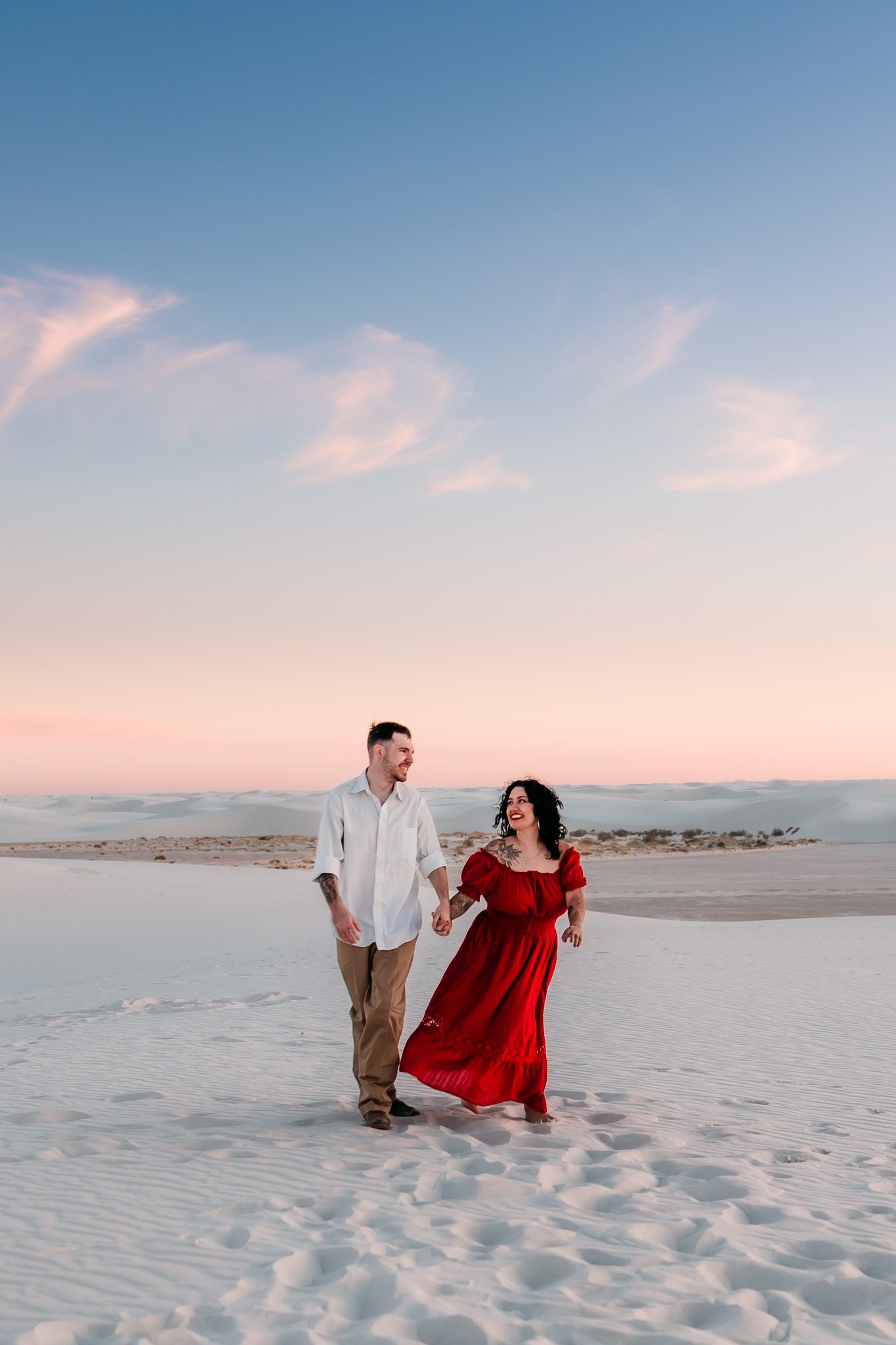 Couple walking hand in hand across the white dunes at sunset during their engagement session at White Sands National Park in New Mexico.