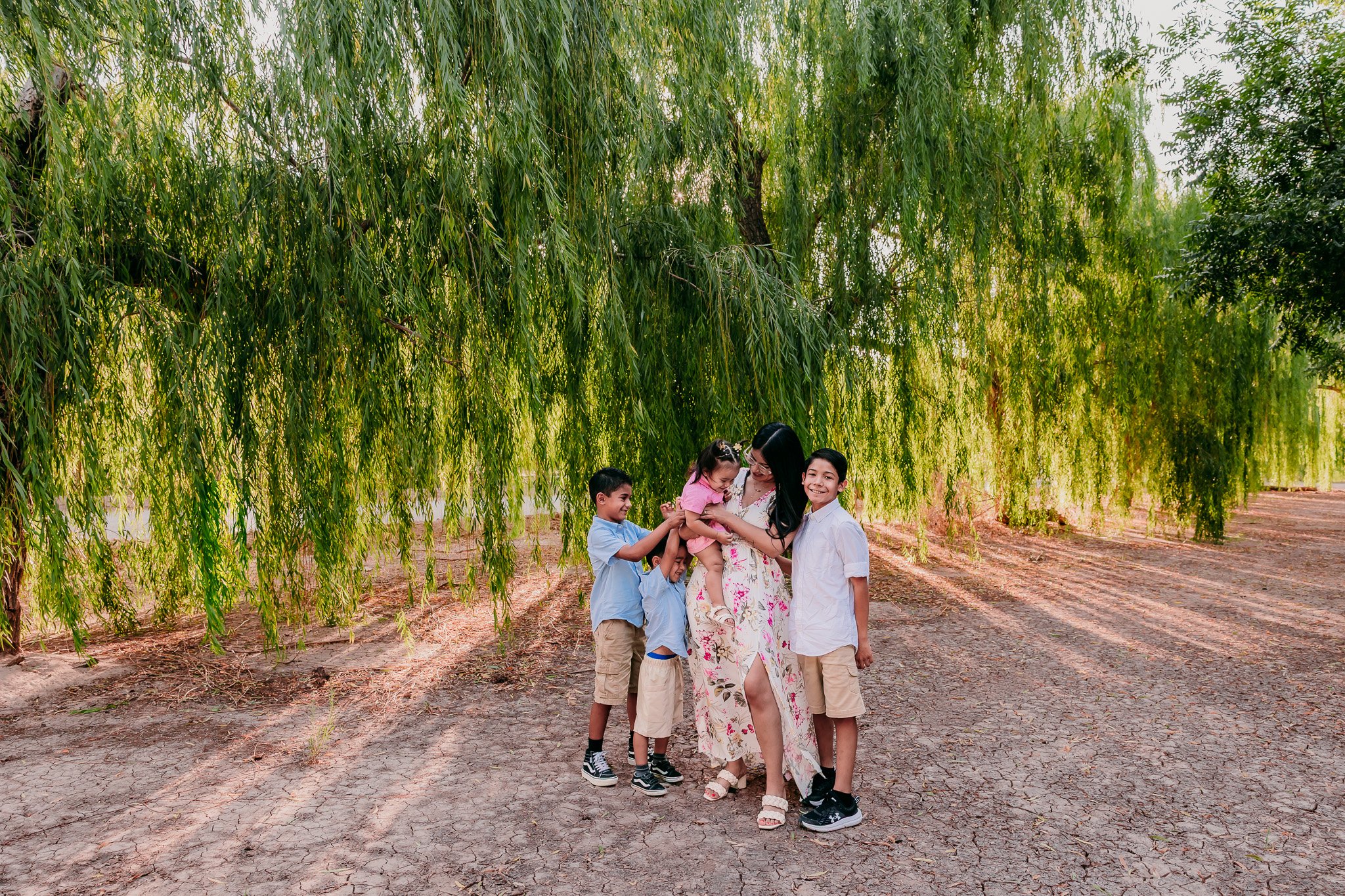 Las Cruces family photographer capturing a family walking beneath willow trees during an outdoor family photography session in Las Cruces, New Mexico.