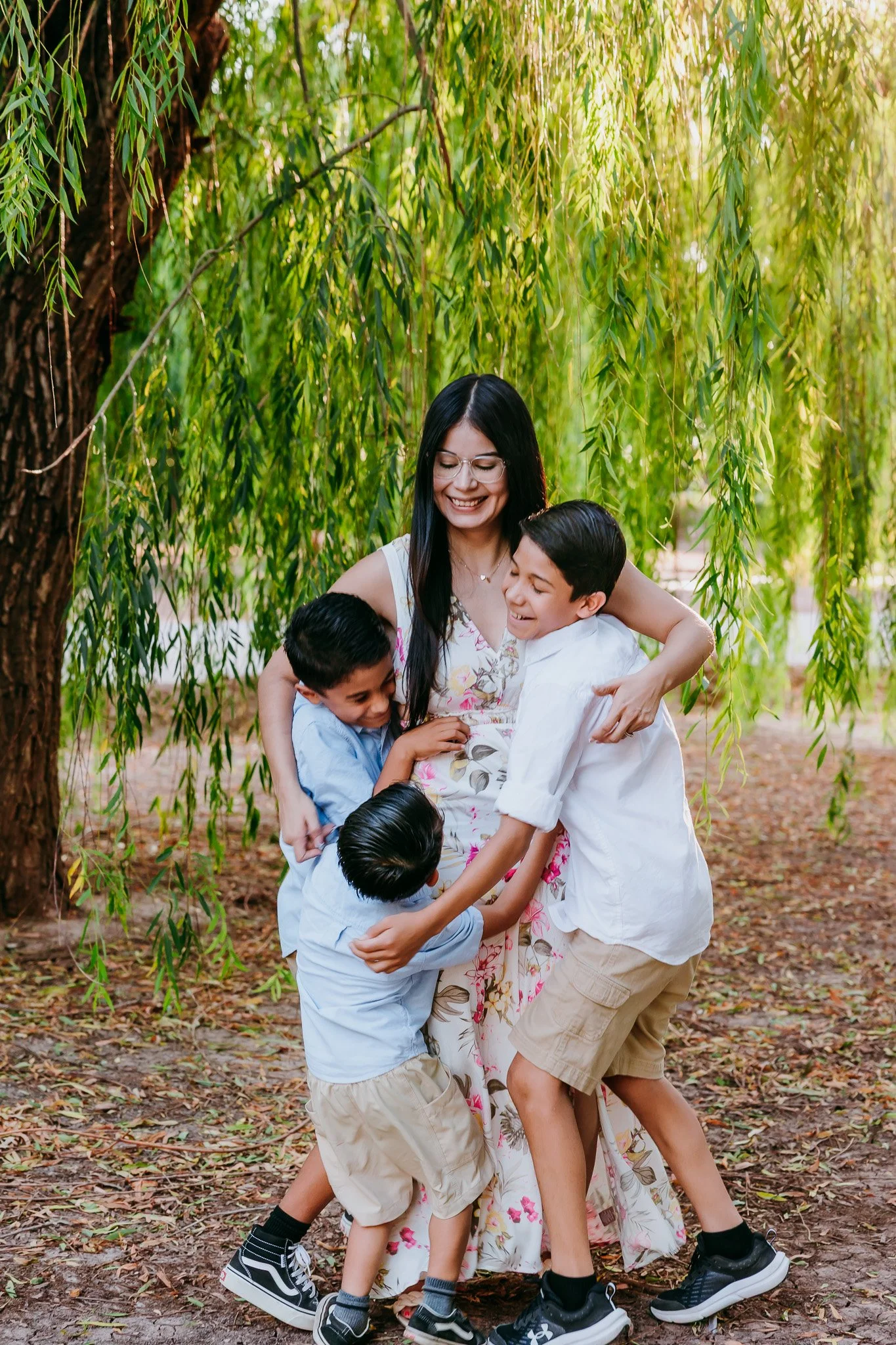 Mother hugging her children beneath willow trees during an outdoor family photography session in Las Cruces.