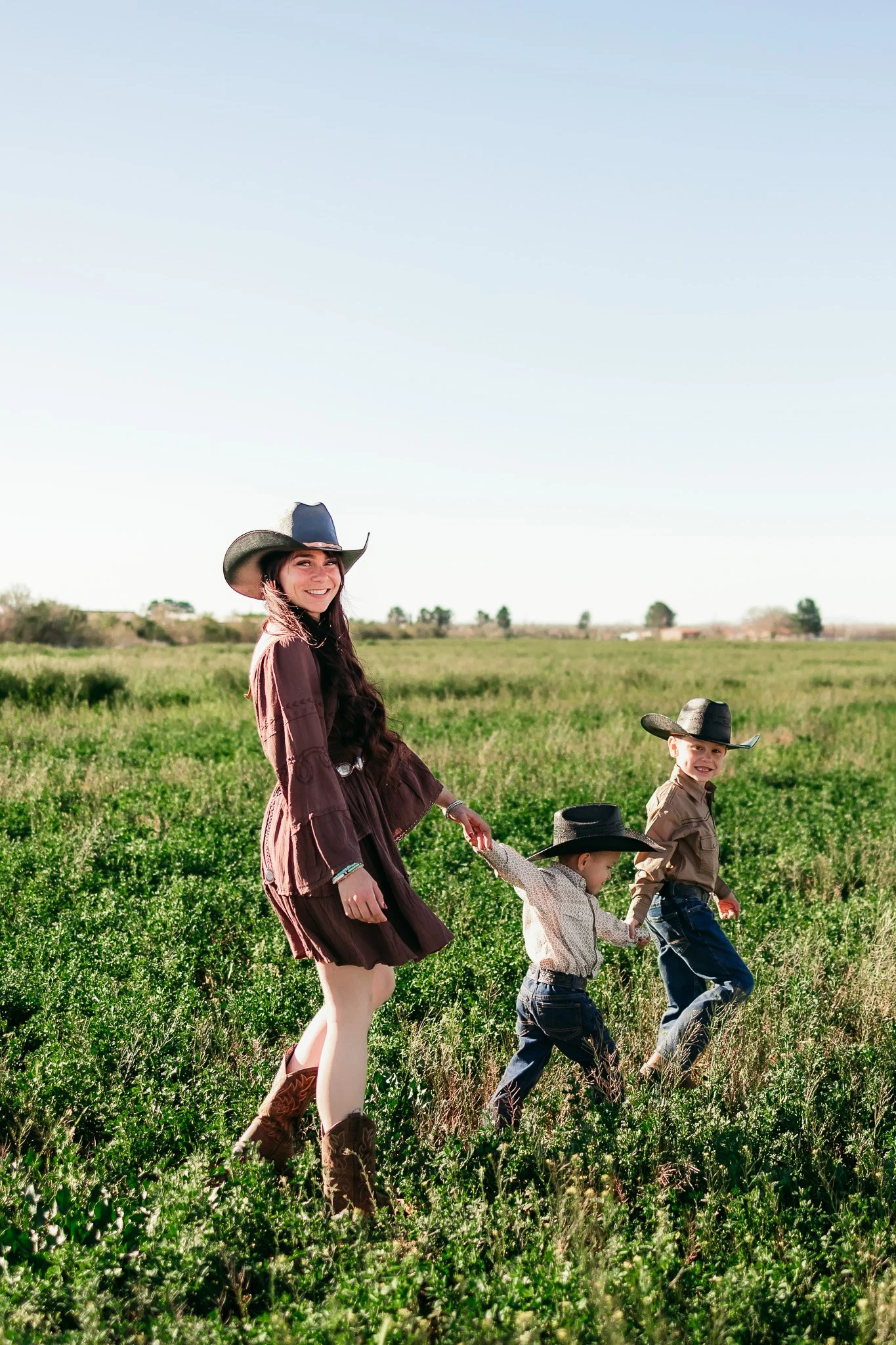 Family walking through a green pasture during a western-inspired outdoor family photography session in southern New Mexico.