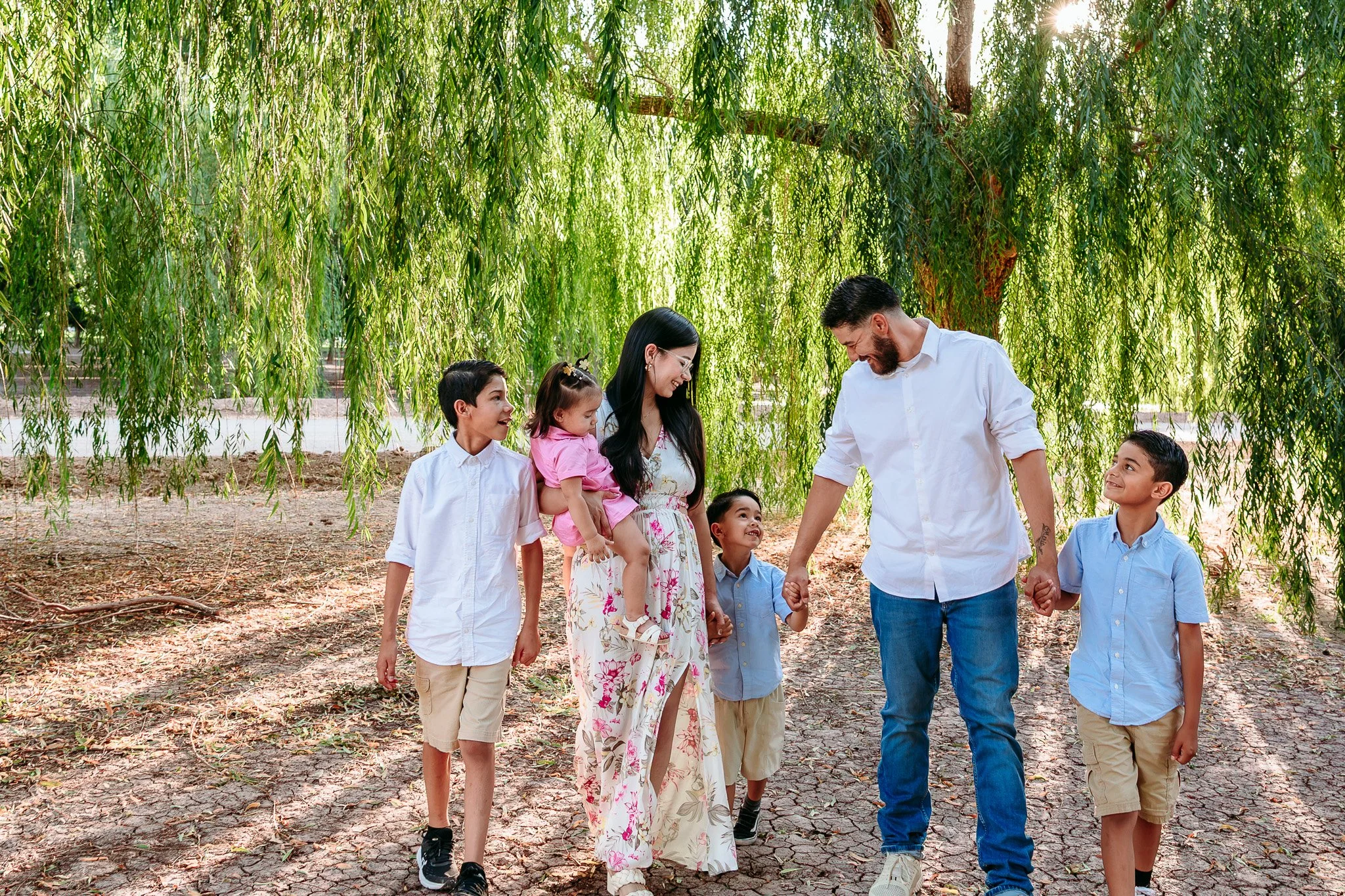 Parents walking hand in hand with their children beneath willow trees during an outdoor family photography session in Las Cruces, New Mexico.