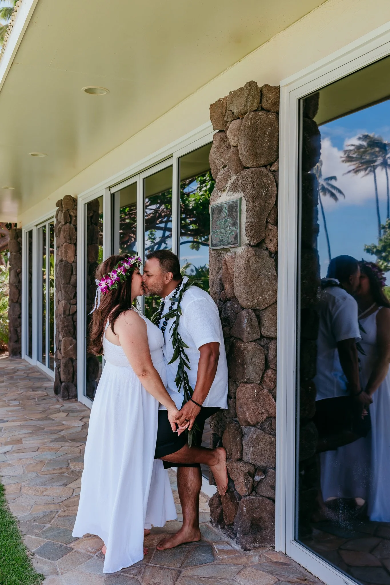 Bride and groom kissing with their reflection in a window overlooking the beach during their Oahu, Hawaii wedding.