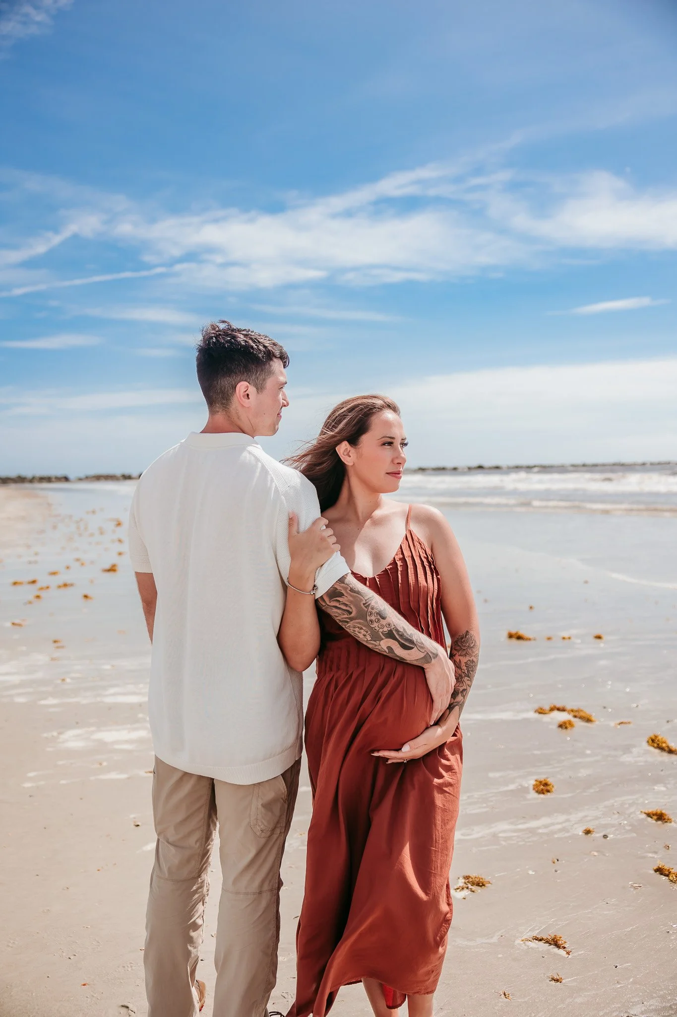 Pregnant mother and father walking together along the shoreline during a maternity photography session in Jacksonville, Florida.