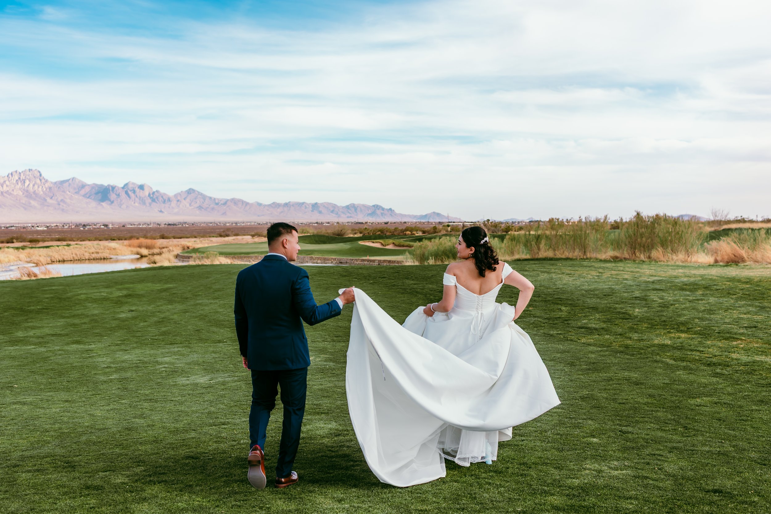 Bride and groom walking across the fairway at Red Hawk Golf Club with the Organ Mountains behind them during their Las Cruces wedding portraits.