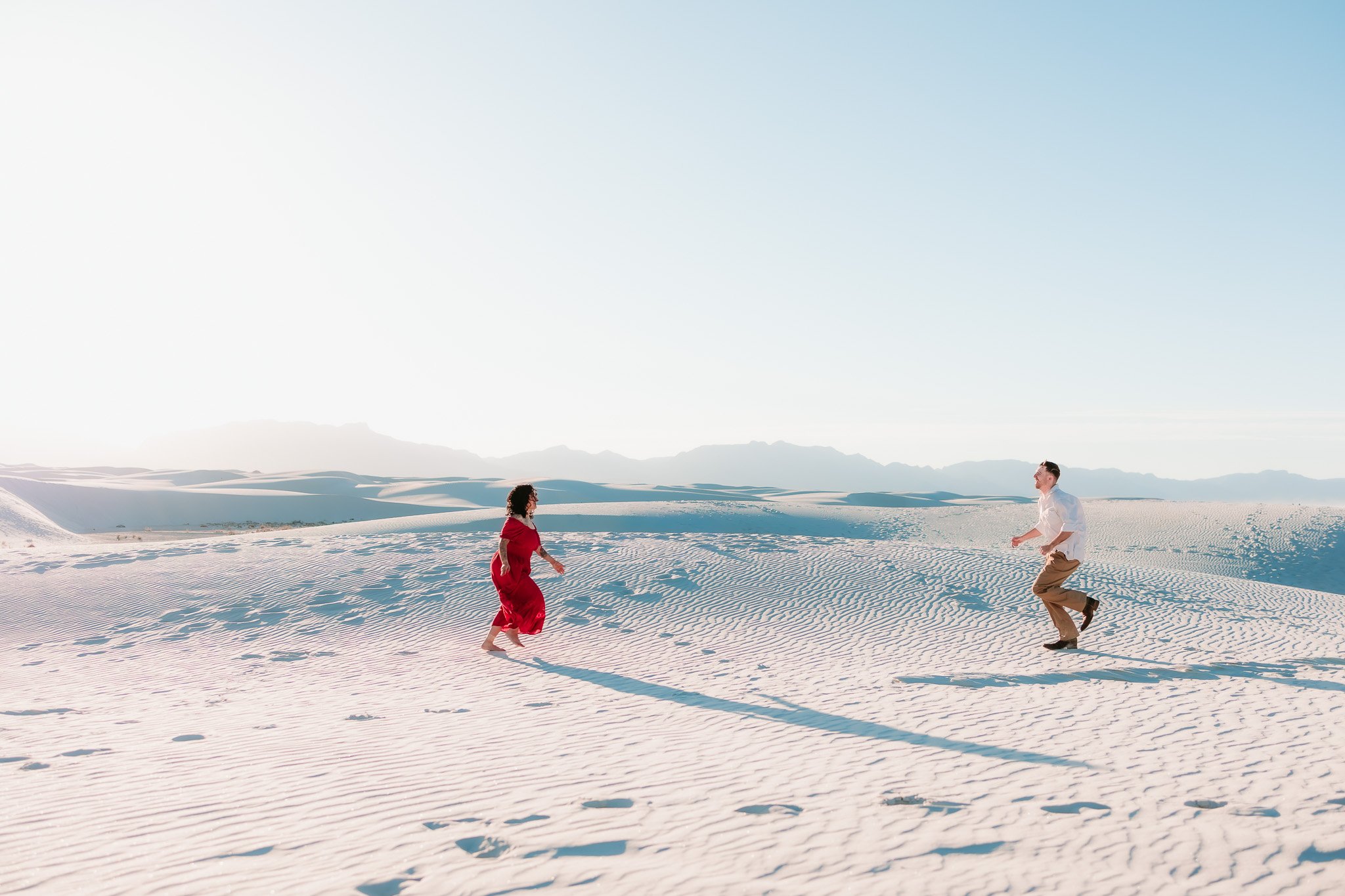 Couple walking across the sweeping white dunes during an adventurous engagement session at White Sands National Park in New Mexico.