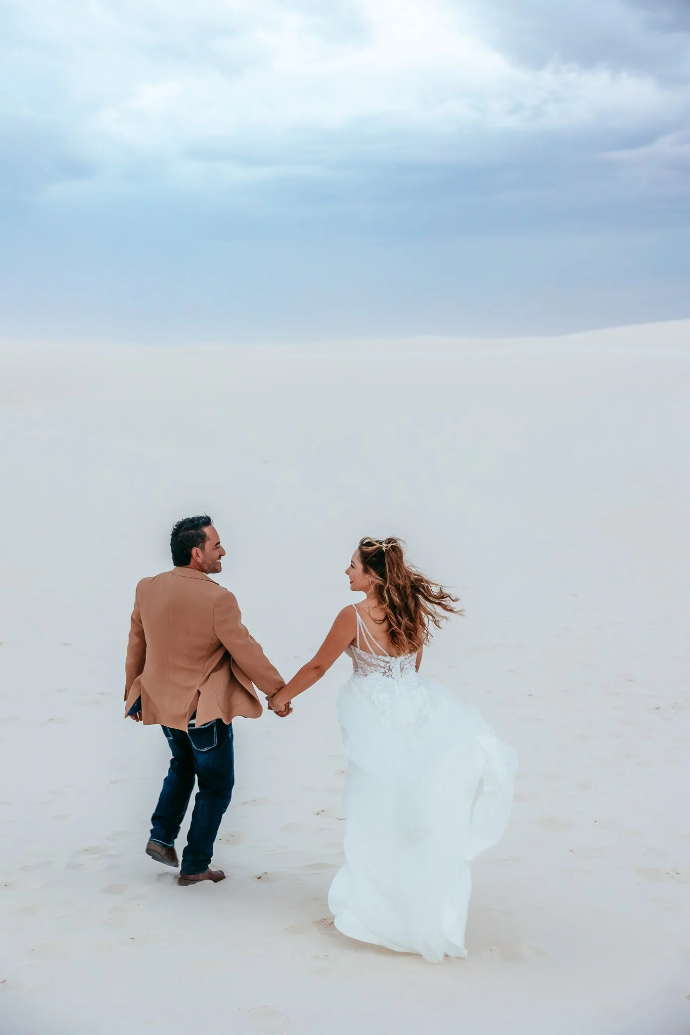 Bride and groom holding hands while walking through the dunes at White Sands National Park in New Mexico.