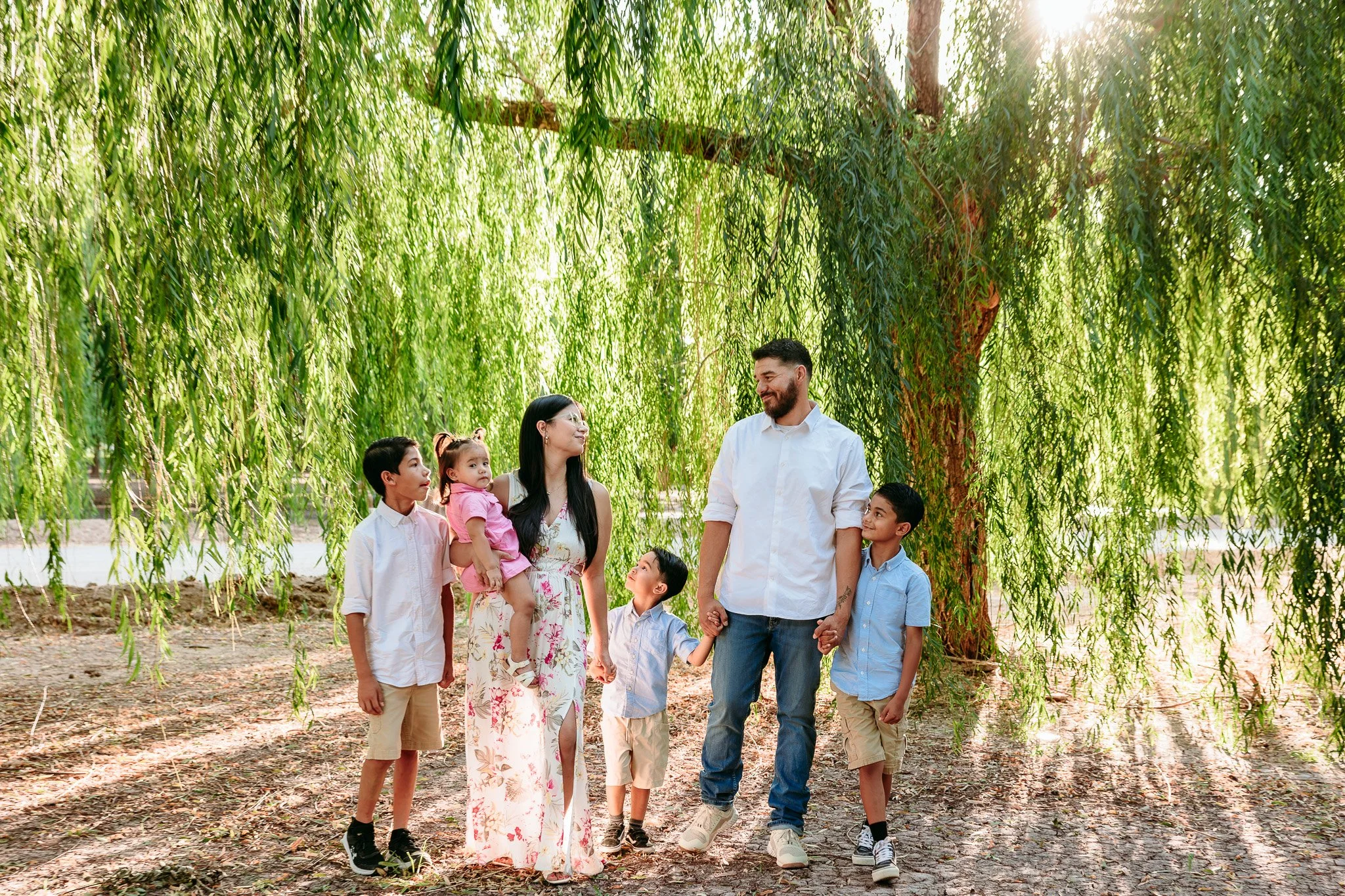 Family standing together beneath willow trees during a natural family photography session in Las Cruces.