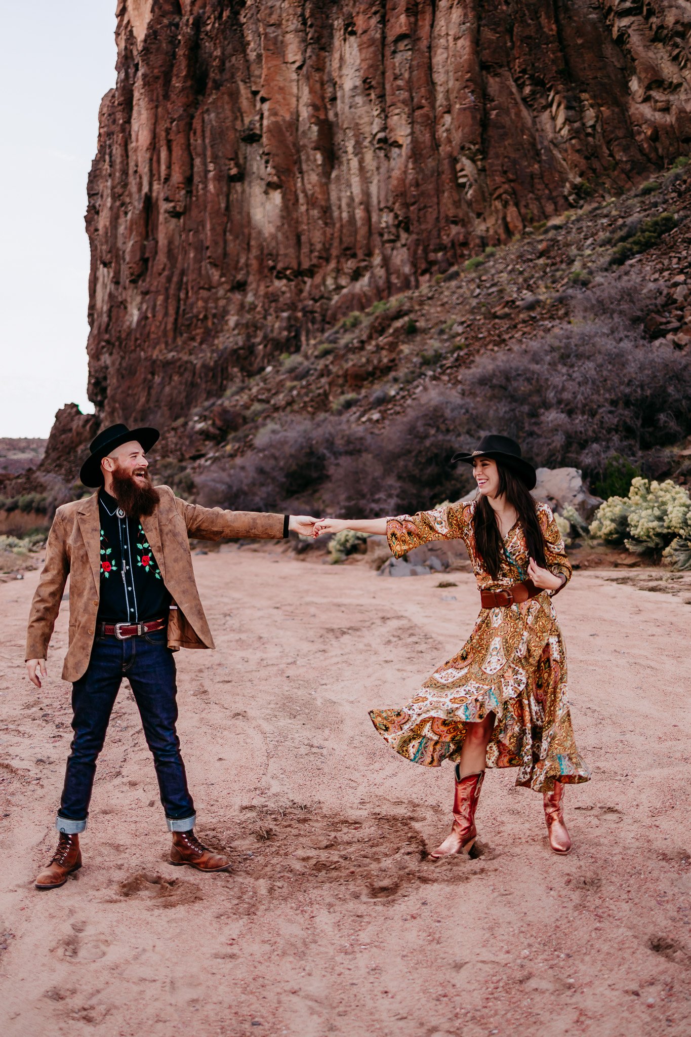 Couple spinning each other beneath towering red rock cliffs at Diablo Canyon near Santa Fe, New Mexico.