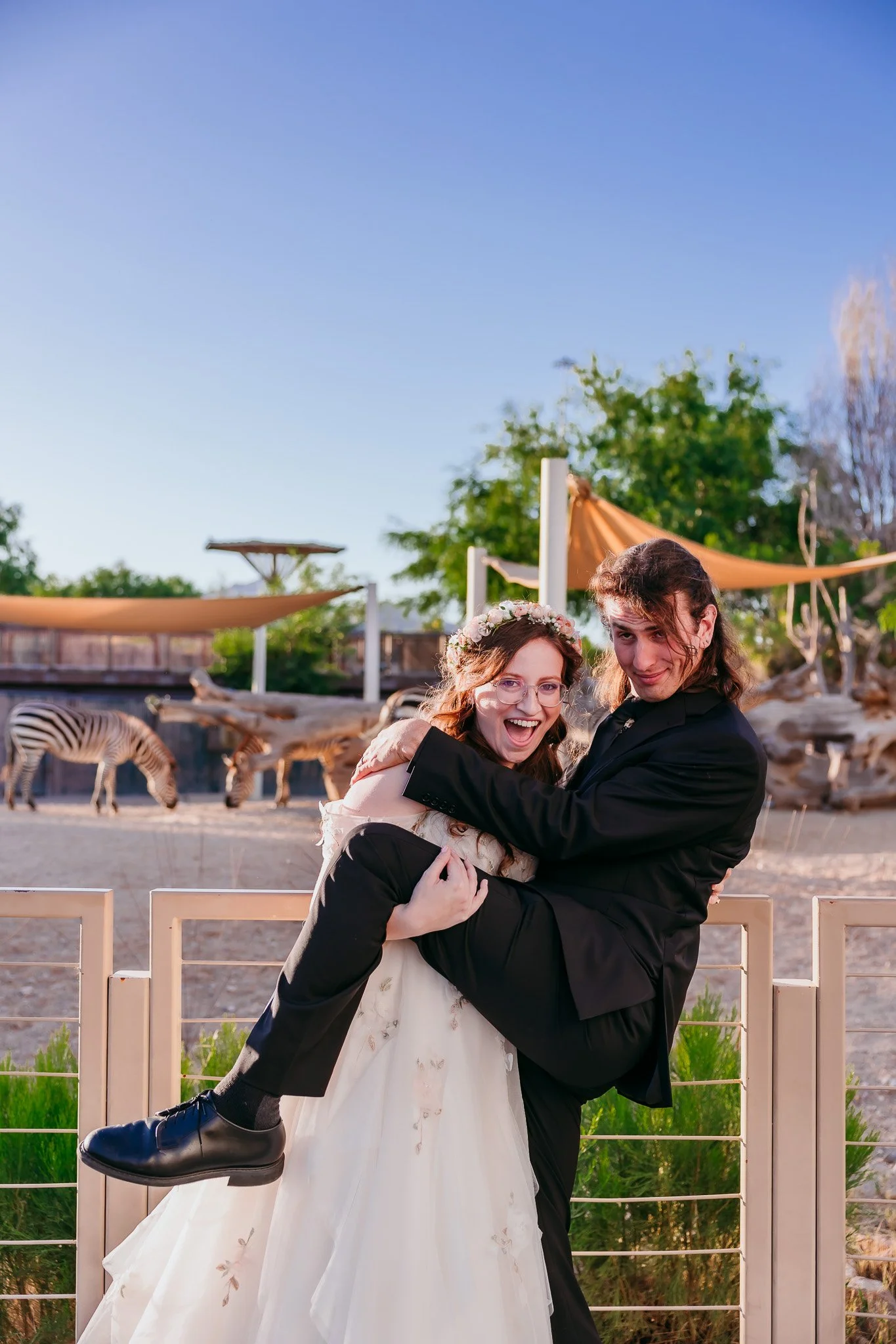 Bride and groom sharing a fun, silly pose with zebras in the background during their wedding at the El Paso Zoo in El Paso, Texas.