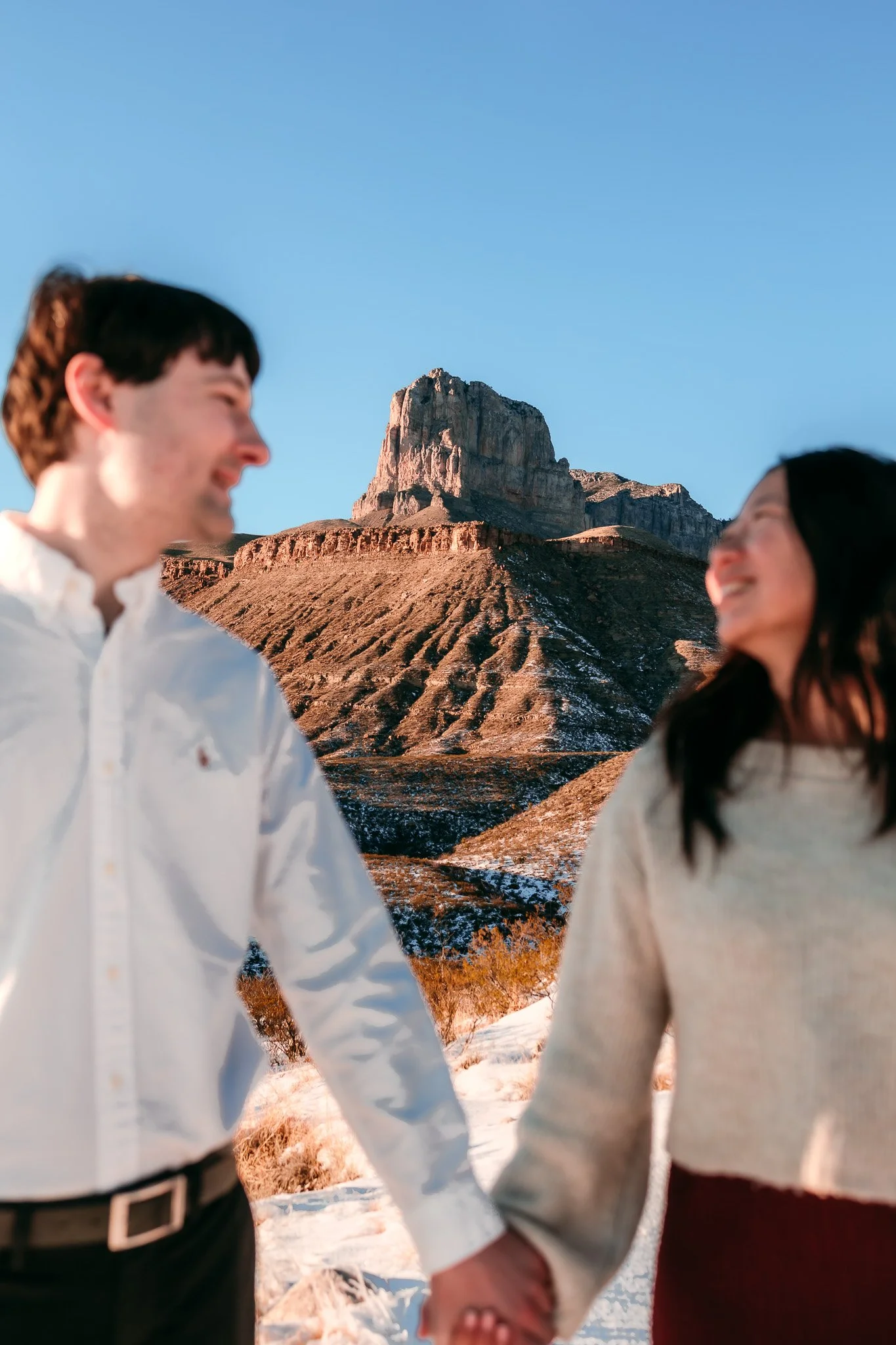 Engaged couple smiling at one another while holding hands during a winter engagement session near the Guadalupe Mountains and Carlsbad, New Mexico.