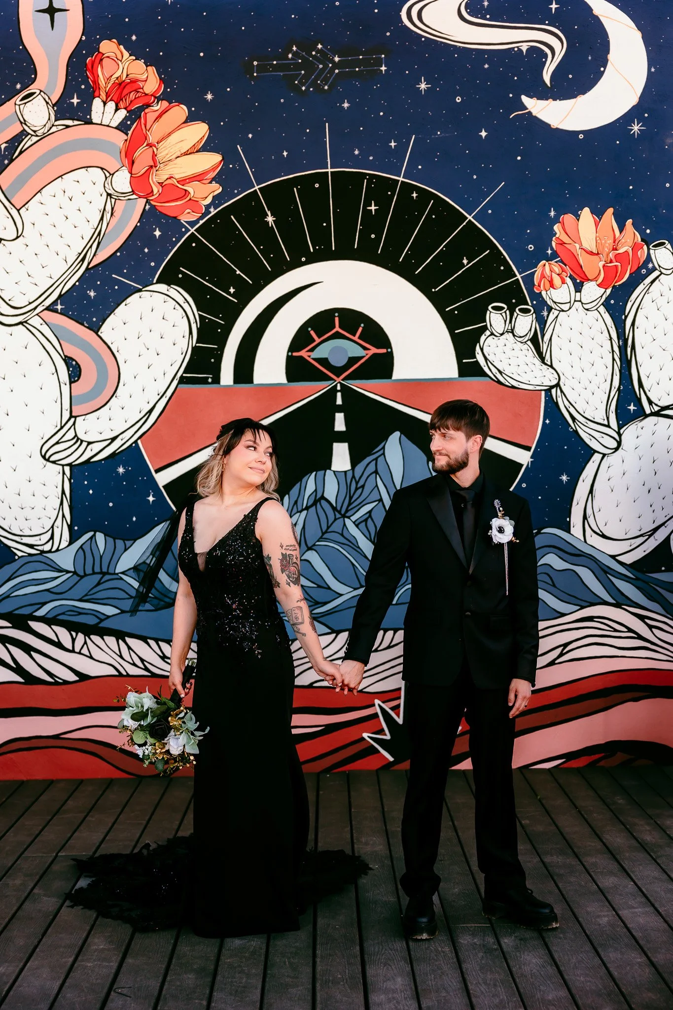 Bride and groom holding hands in front of the iconic desert mural at The Mystic during their intimate wedding in Santa Fe, New Mexico.