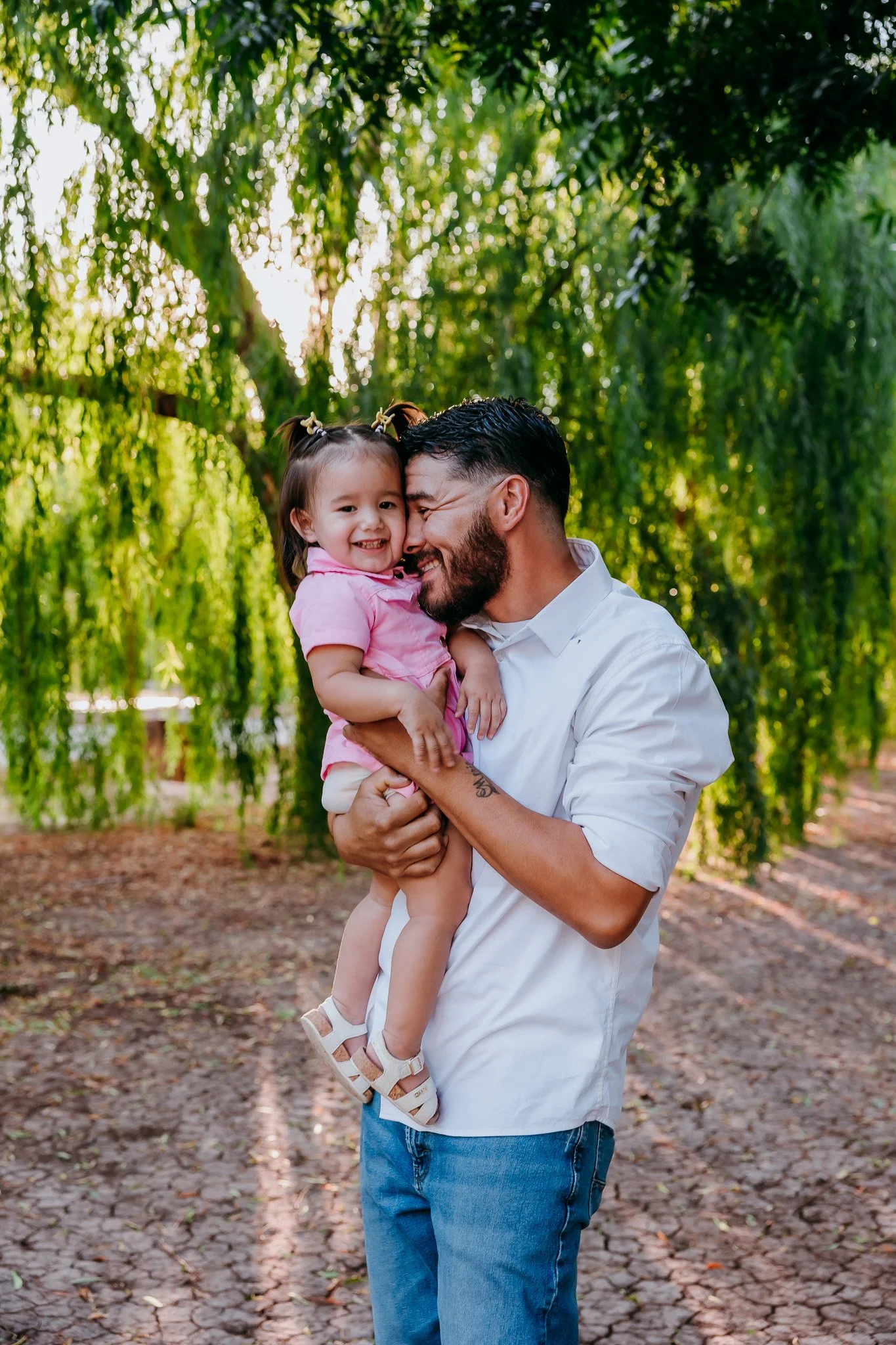 Father holding his daughter beneath willow trees during a candid family photography session in Las Cruces, New Mexico.