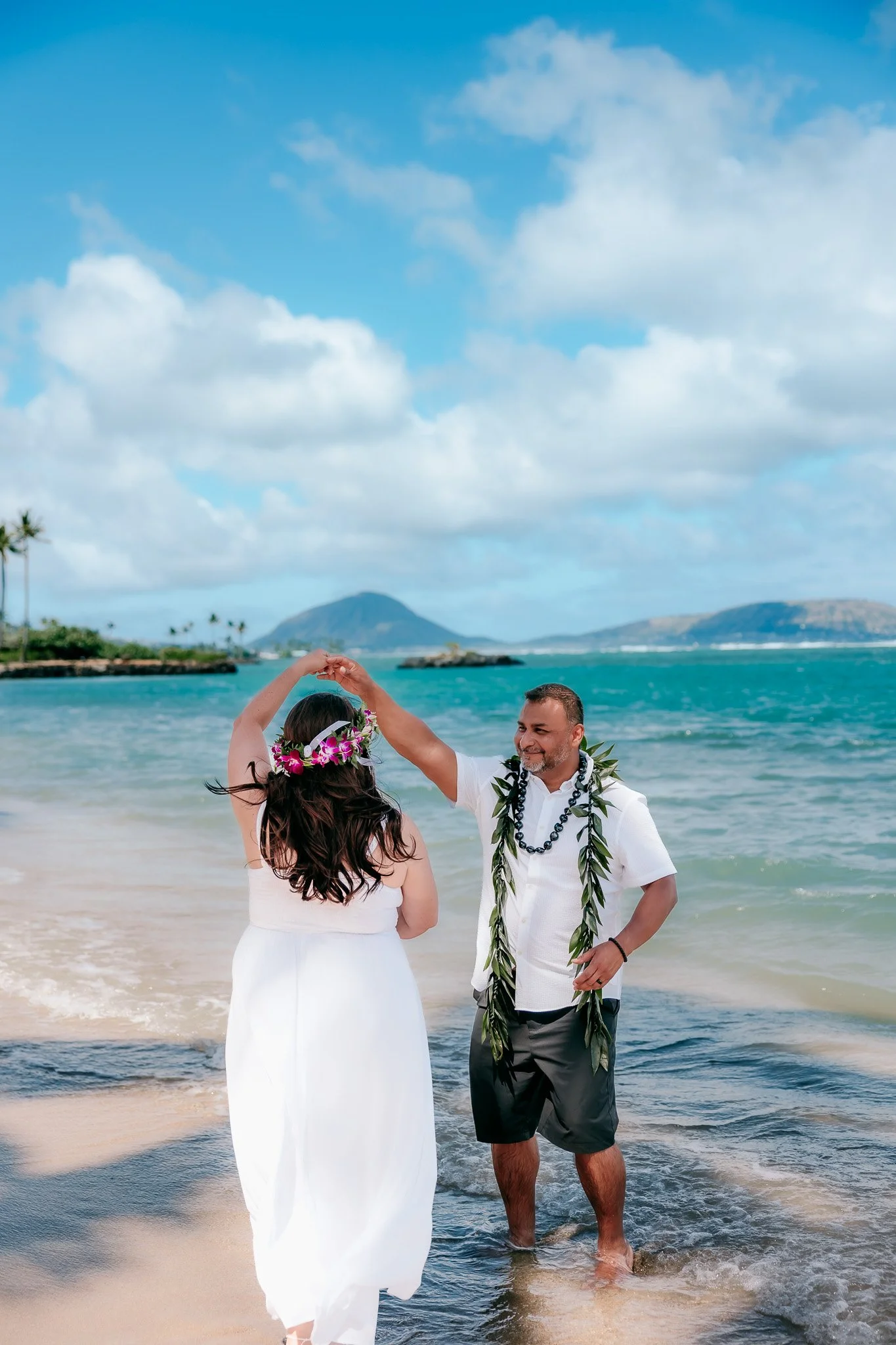 Newlyweds dancing together on the beach shore during their destination wedding on Oahu, Hawaii.